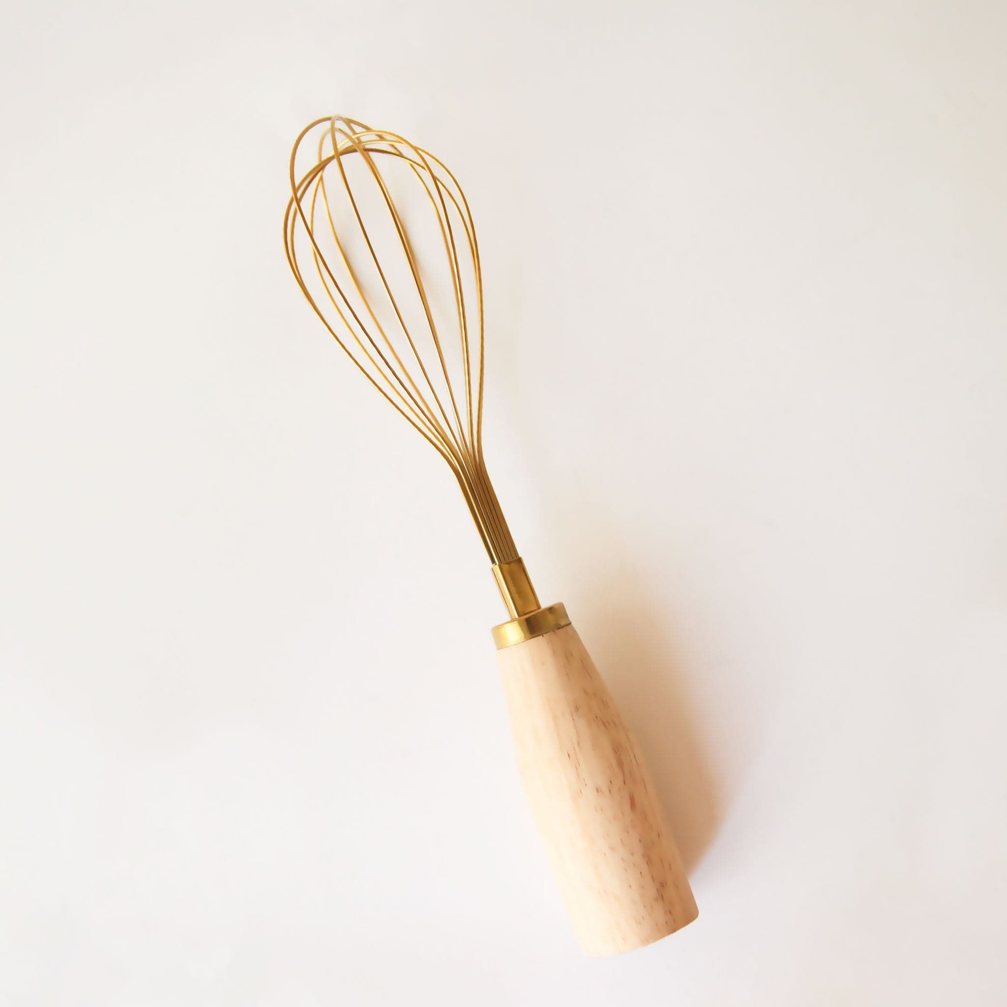 On a white background is a gold whisk with a wood handle. 