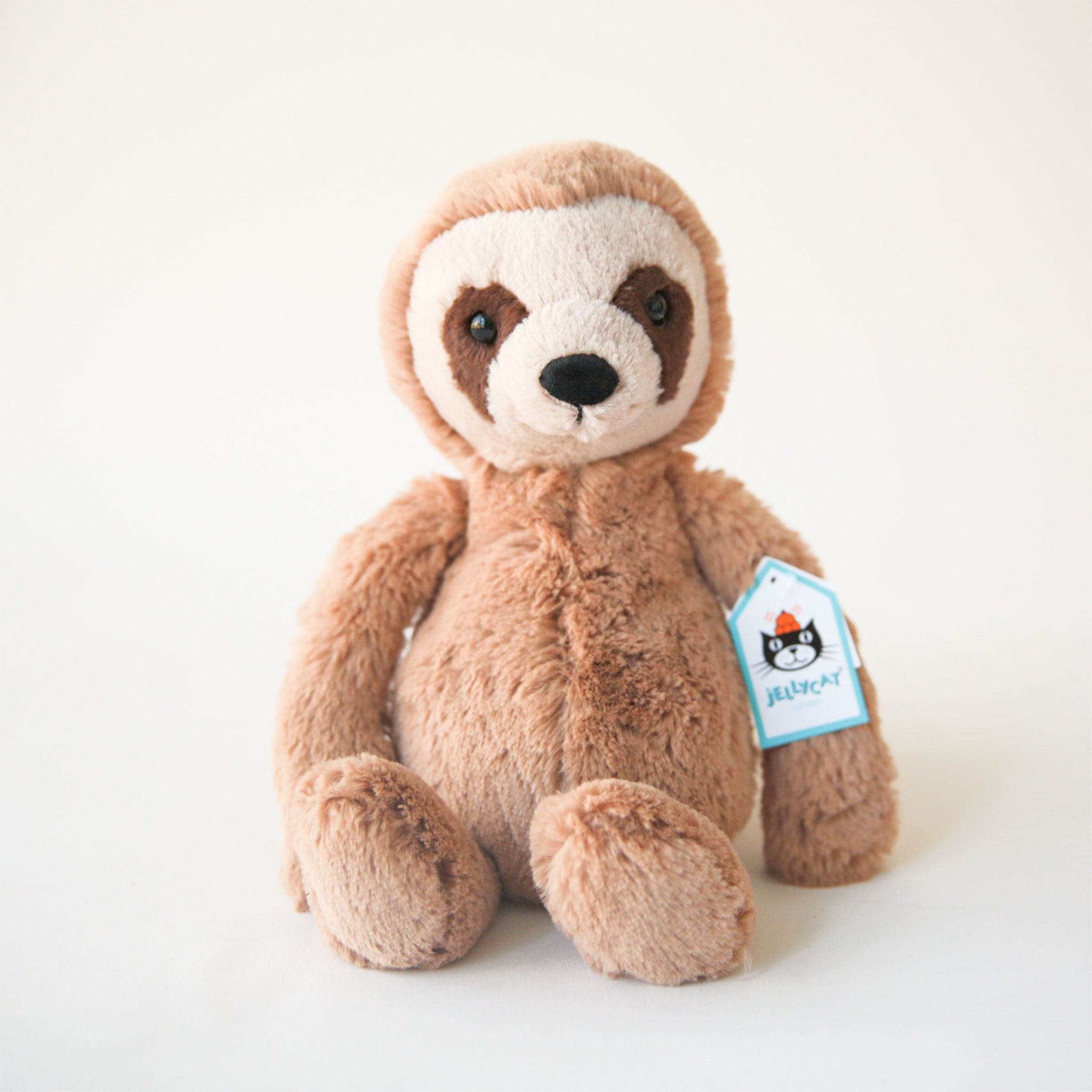 A fuzzy brown sloth stuffed animal with darker brown markings around his eyes, a cream colored face and a black nose.