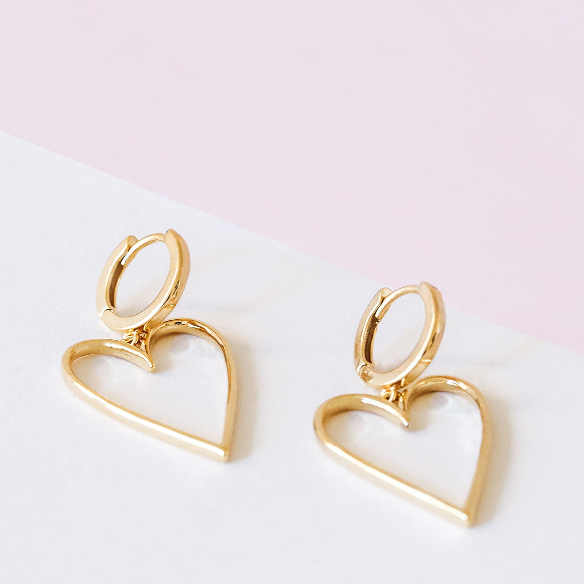 A pair of gold hoop earrings with a larger hold heart shape hoop attached to that.