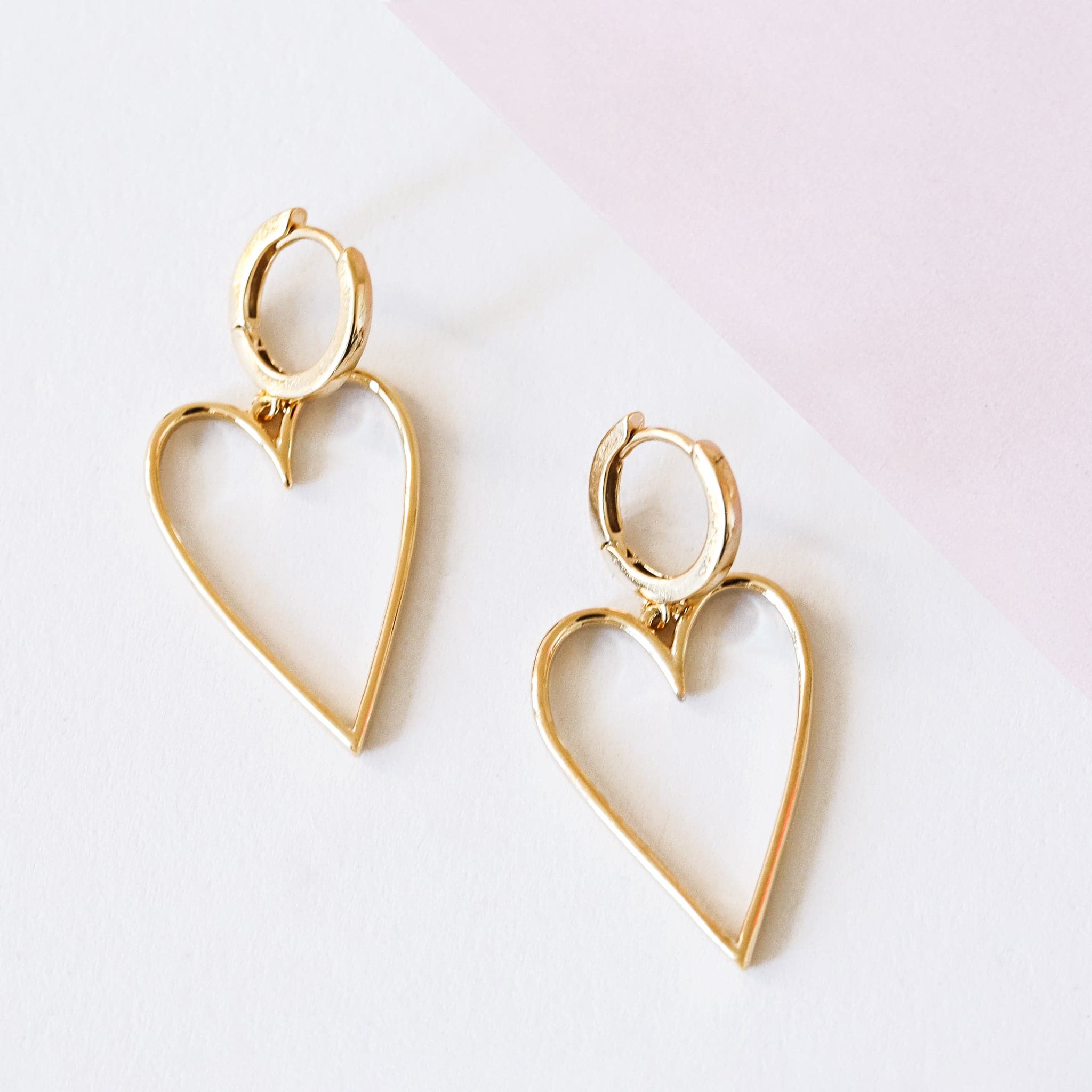 A pair of gold hoop earrings with a larger hold heart shape hoop attached to that.