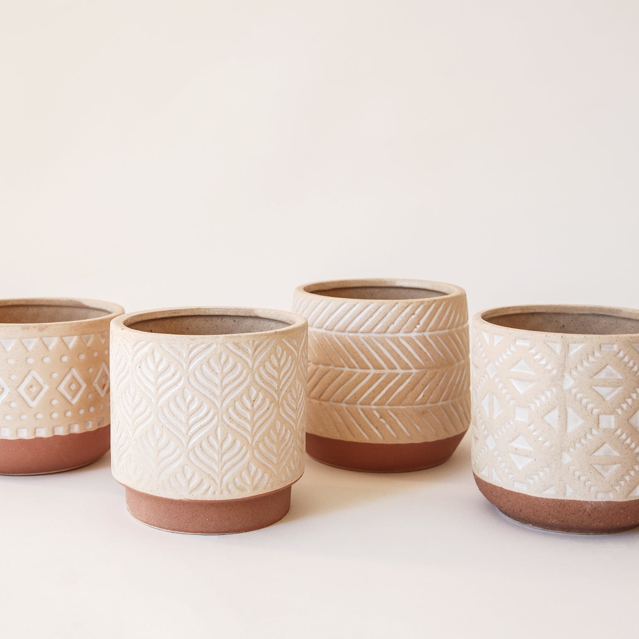 Each pot type shown. The bottom of the vessel is a dark tan while the top color is lighter with white imprinted designs.