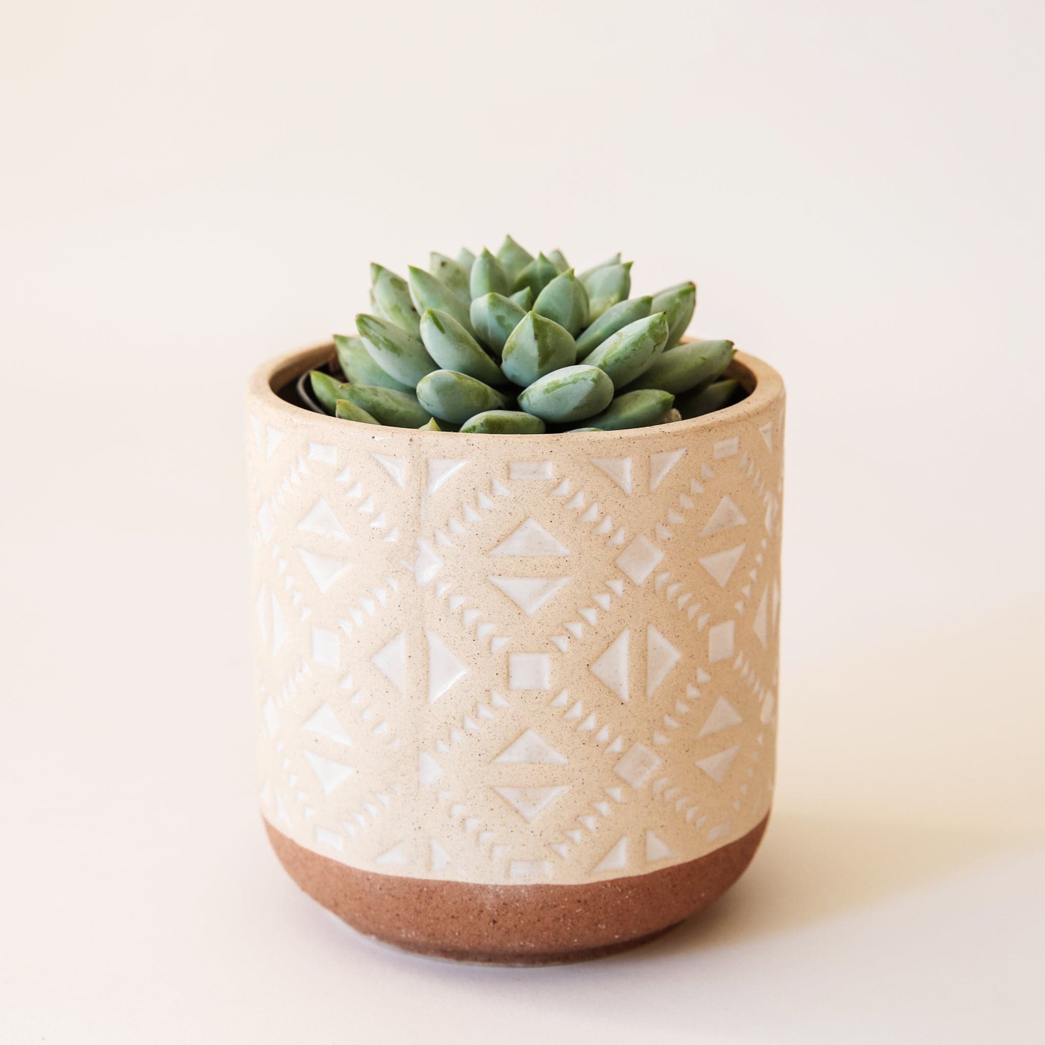 A pot where the bottom tapers and us rounded The bottom of the vessel is a dark tan while the top color is lighter with white imprinted aztec inspired triangle designs.