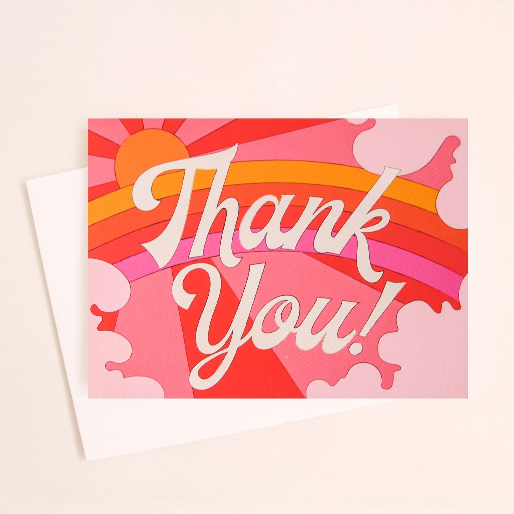 Card with a vibrant scene of a rosie toned rainbow and beaming pink and red sun. Soft pink cloud take up the edges. The center of the card reads &#39;Thank you!&#39; in white cursive lettering.