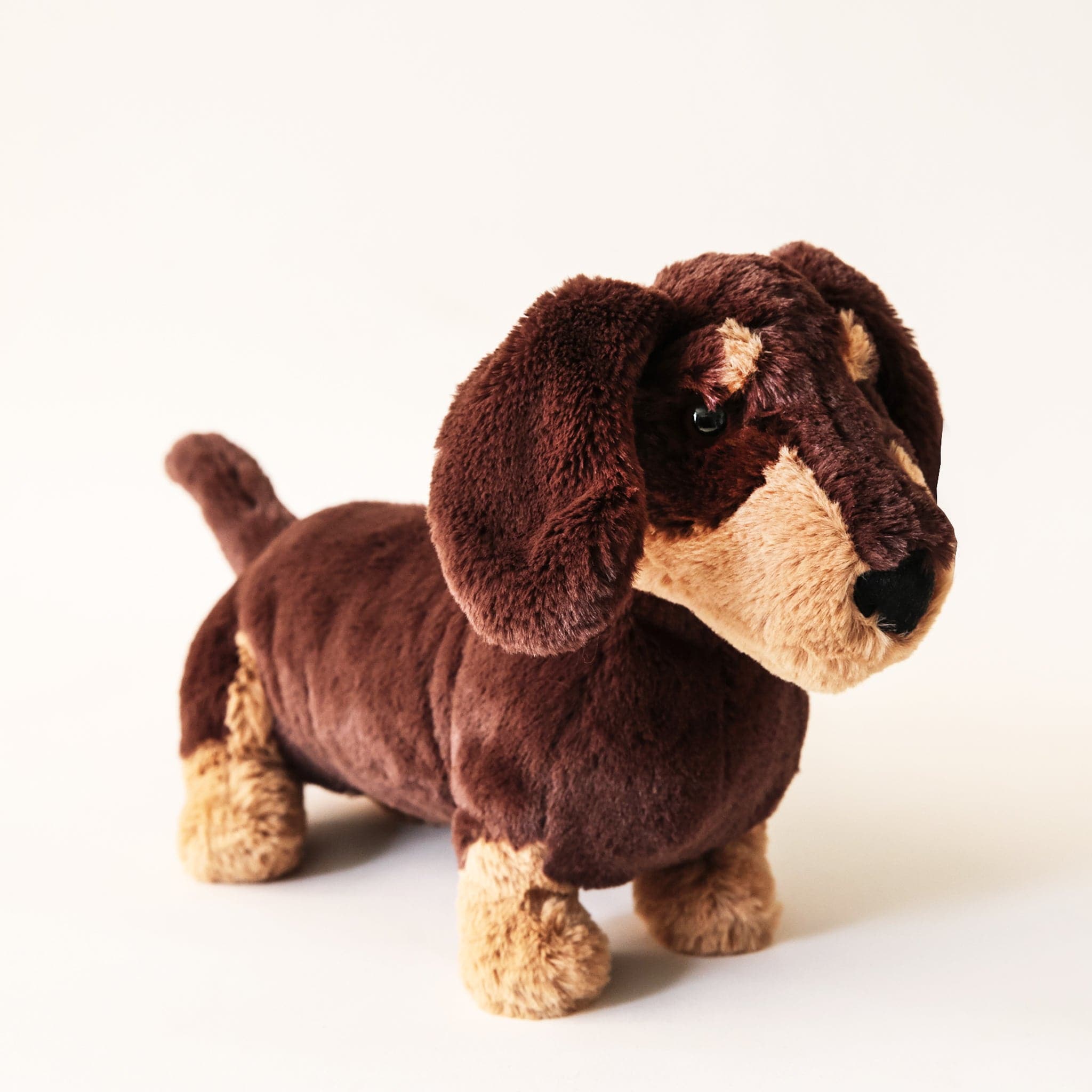 Soft stuffed animal in the shape of a dark chocolate colored dachshund Weiner dog with caramel colored spots.