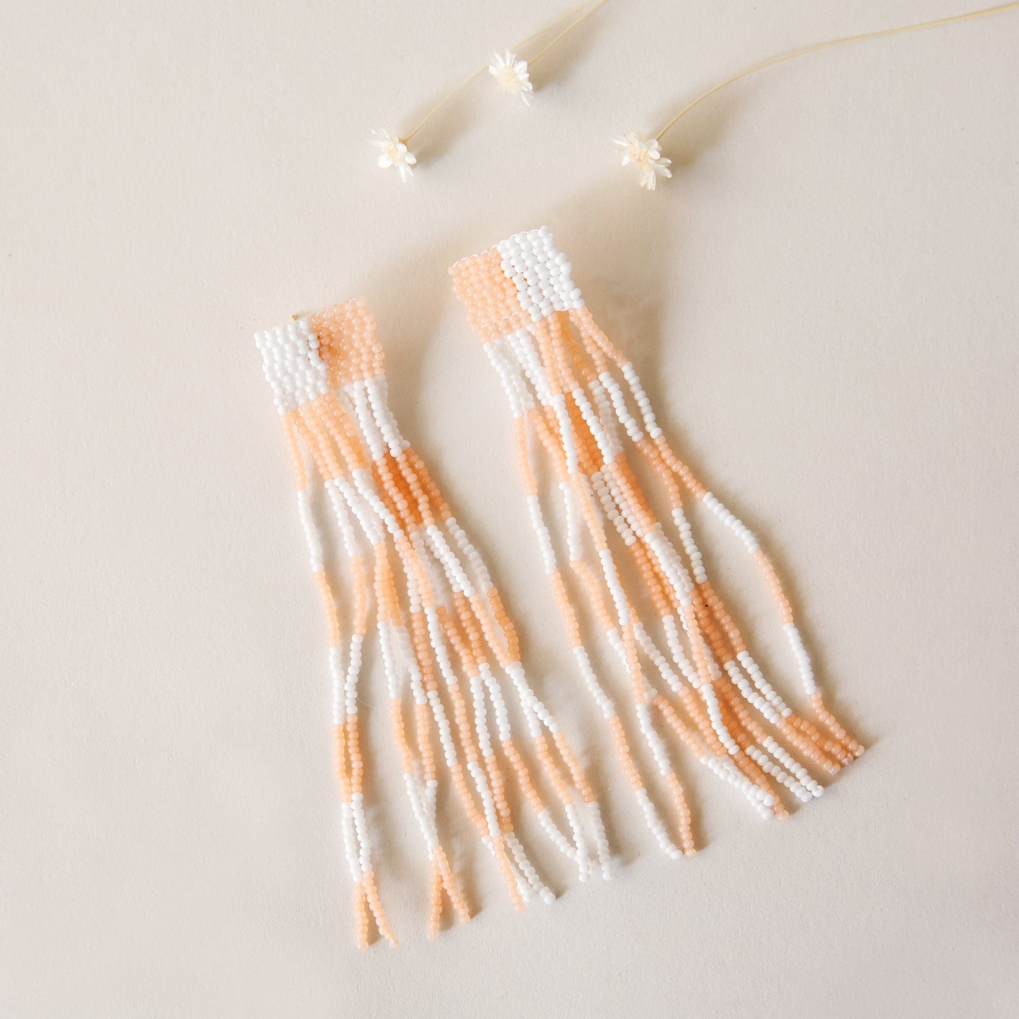 Beaded peach and white earrings with a checker design. They have long dangling beaded strings that make for a fun addition to any outfit.