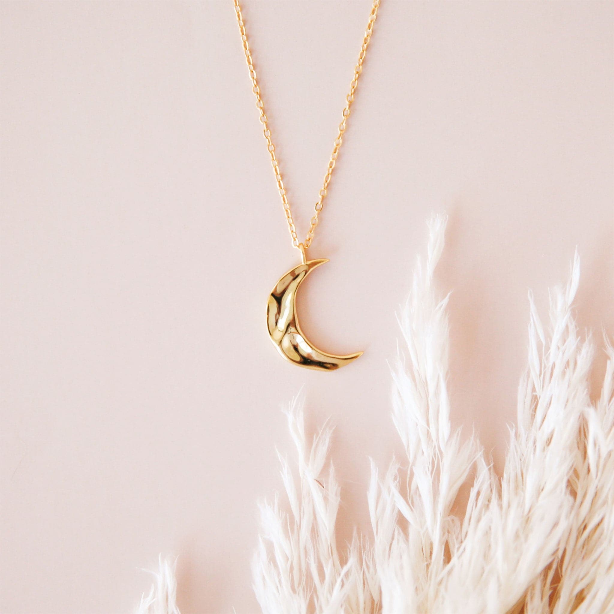 A gold dainty necklace with a crescent moon pendant with a wavy texture.