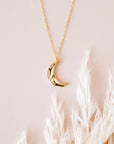 A gold dainty necklace with a crescent moon pendant with a wavy texture.