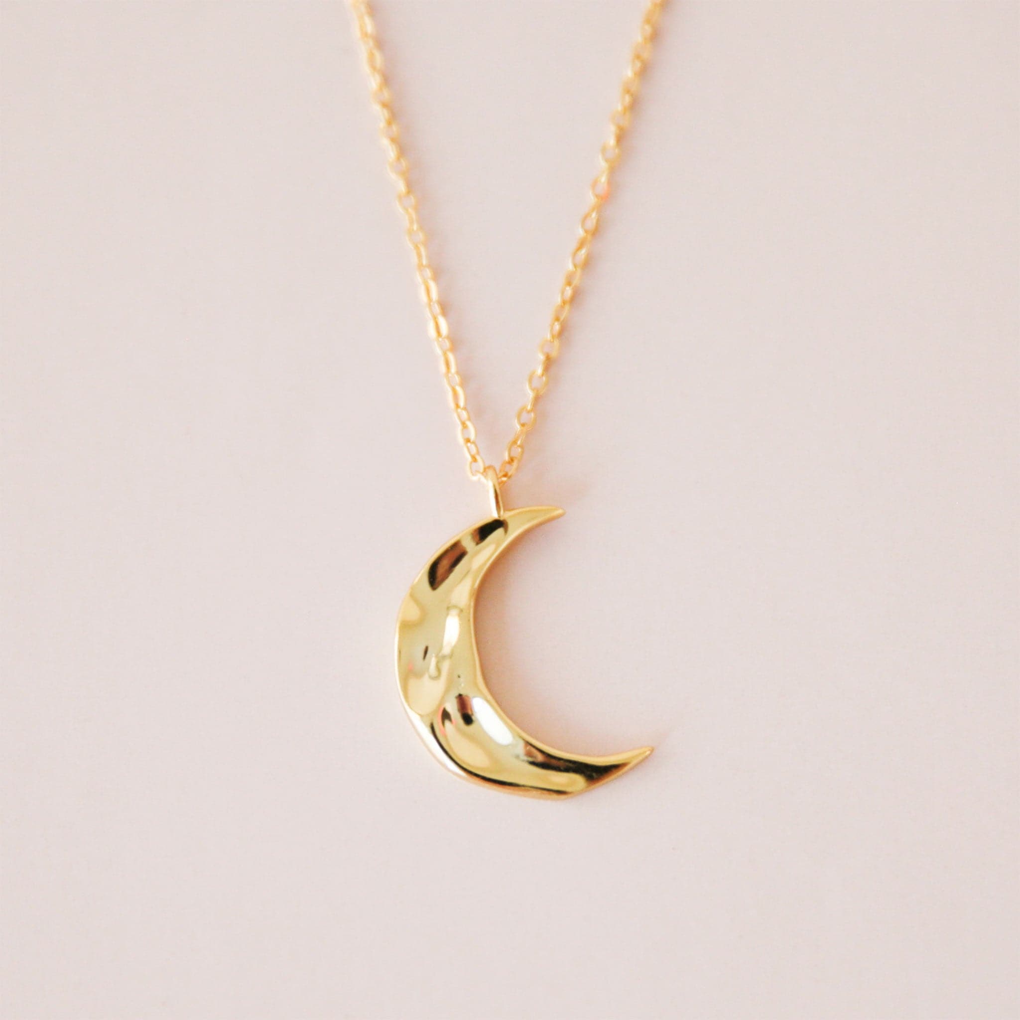 A gold dainty necklace with a crescent moon pendant with a wavy texture.