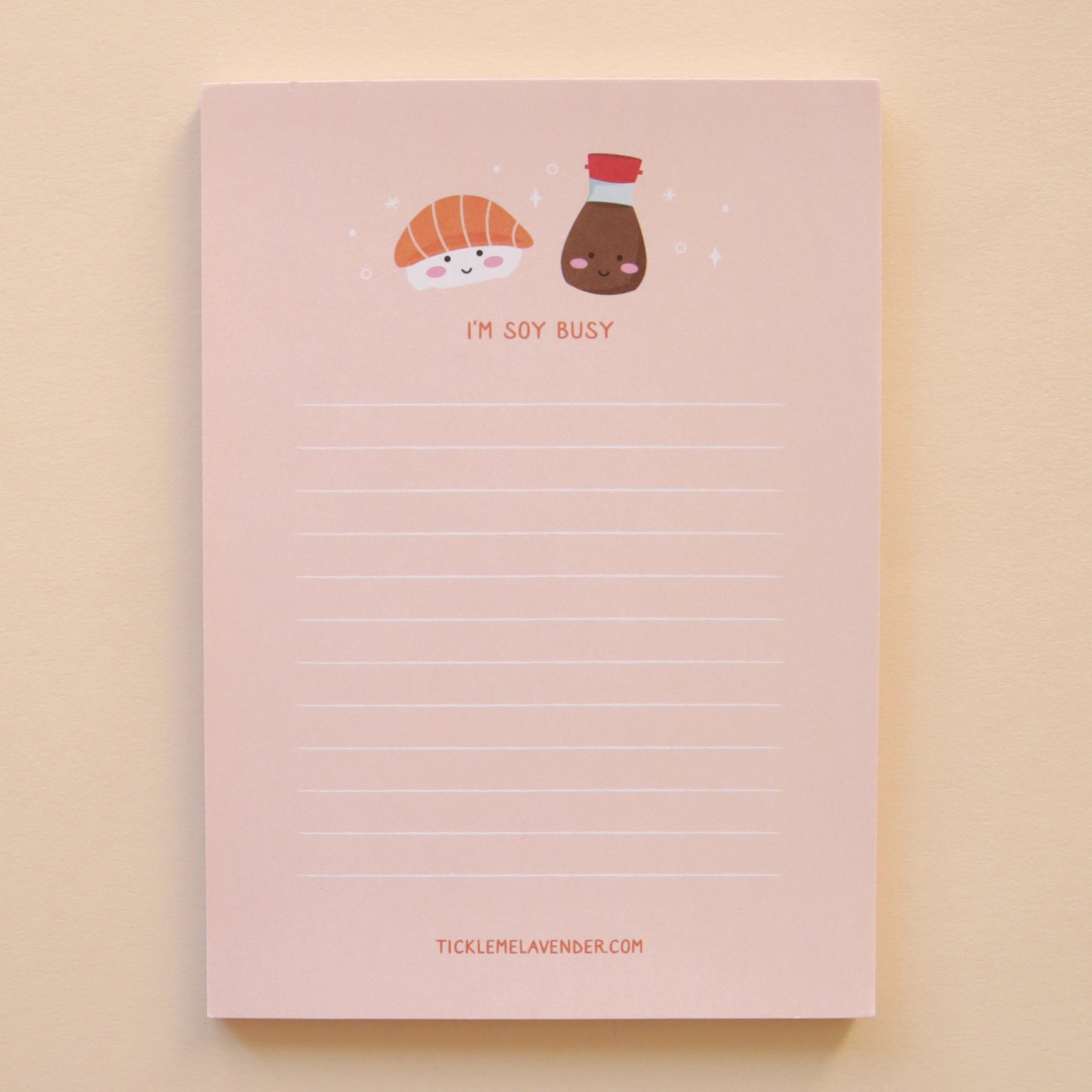 A light pink notepad with white lines for writing and a salmon sashimi and soy sauce graphic at the top along with orange letters underneath that read, &quot;I&#39;m Soy Busy&quot;.