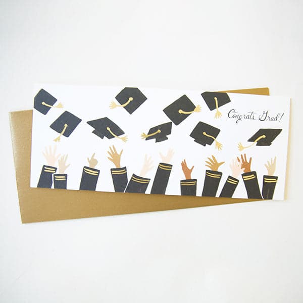On a white background is a card with a bunch of hands throwing up graduation caps along with text in the right corner that reads, "Congrats Grad!" as well as a coordinating gold envelope. 