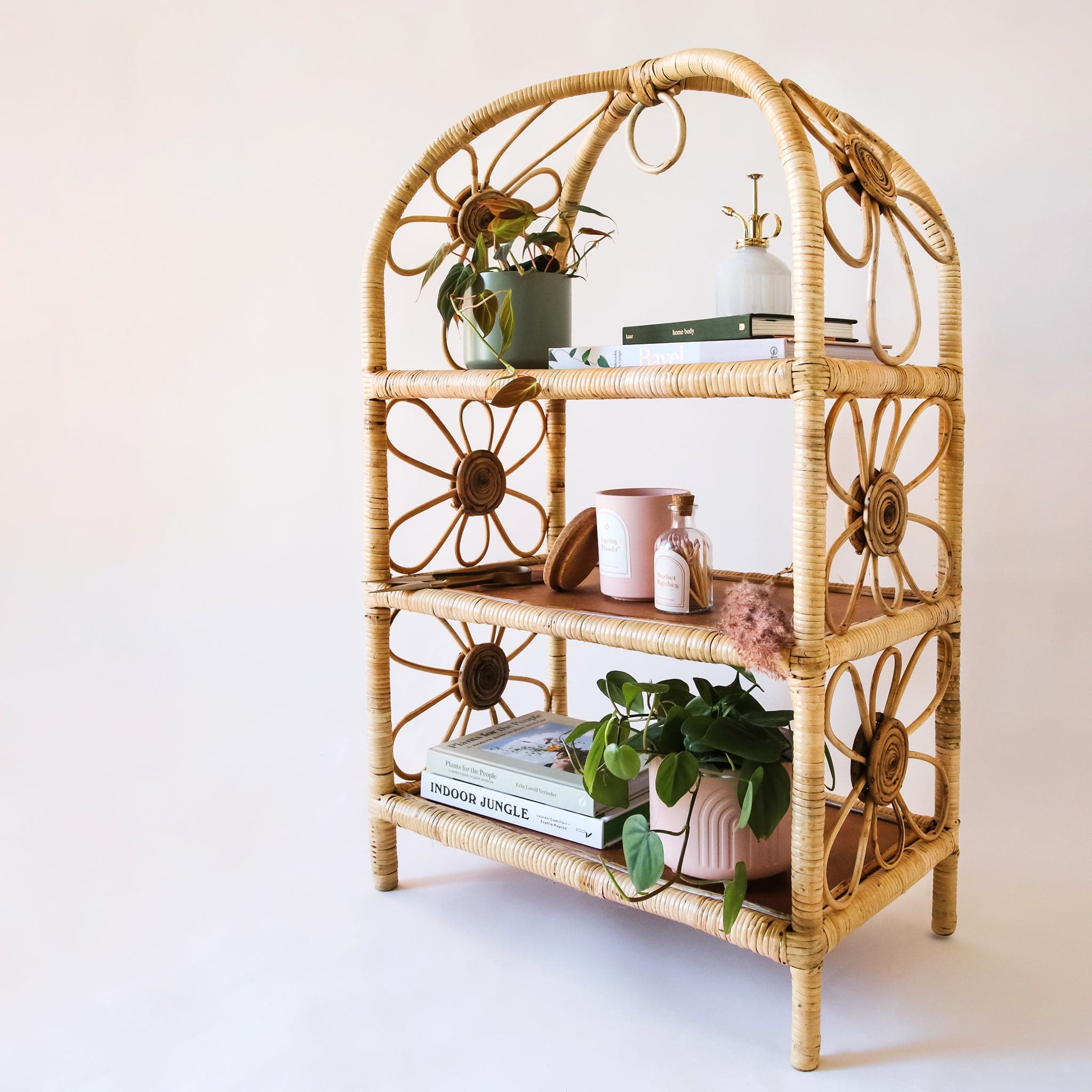 Natural woven rattan shelf with daisy accents on both sides. The sides are open and let in ample light to keep the shelves well lit. Displayed on each shelf are plants, books and little treasures.