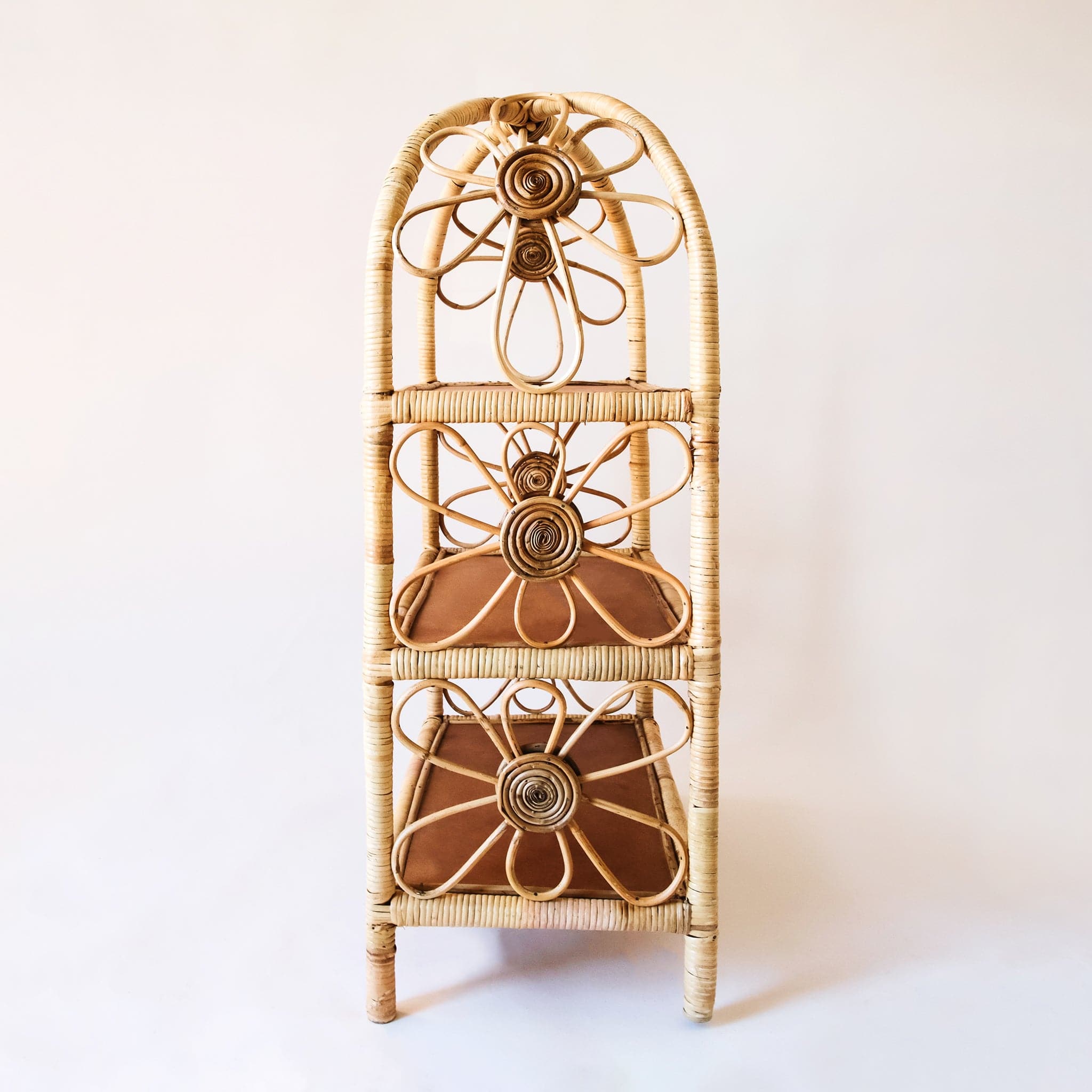 Side view of natural woven rattan shelf with daisy accents on both sides. The sides are open and let in ample light to keep the shelves well lit. Each shelf is covered in rattan and has a chocolate brown bottom.
