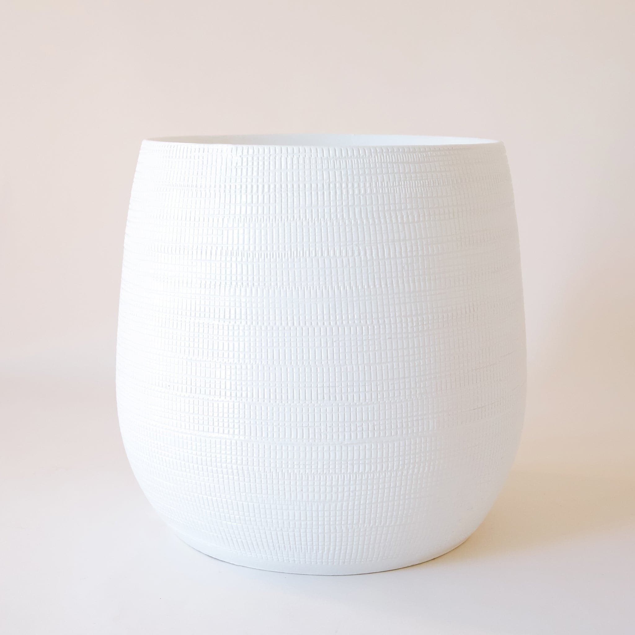 On a cream background is a white rounded ceramic pot with a tiny rectangular texture all over.