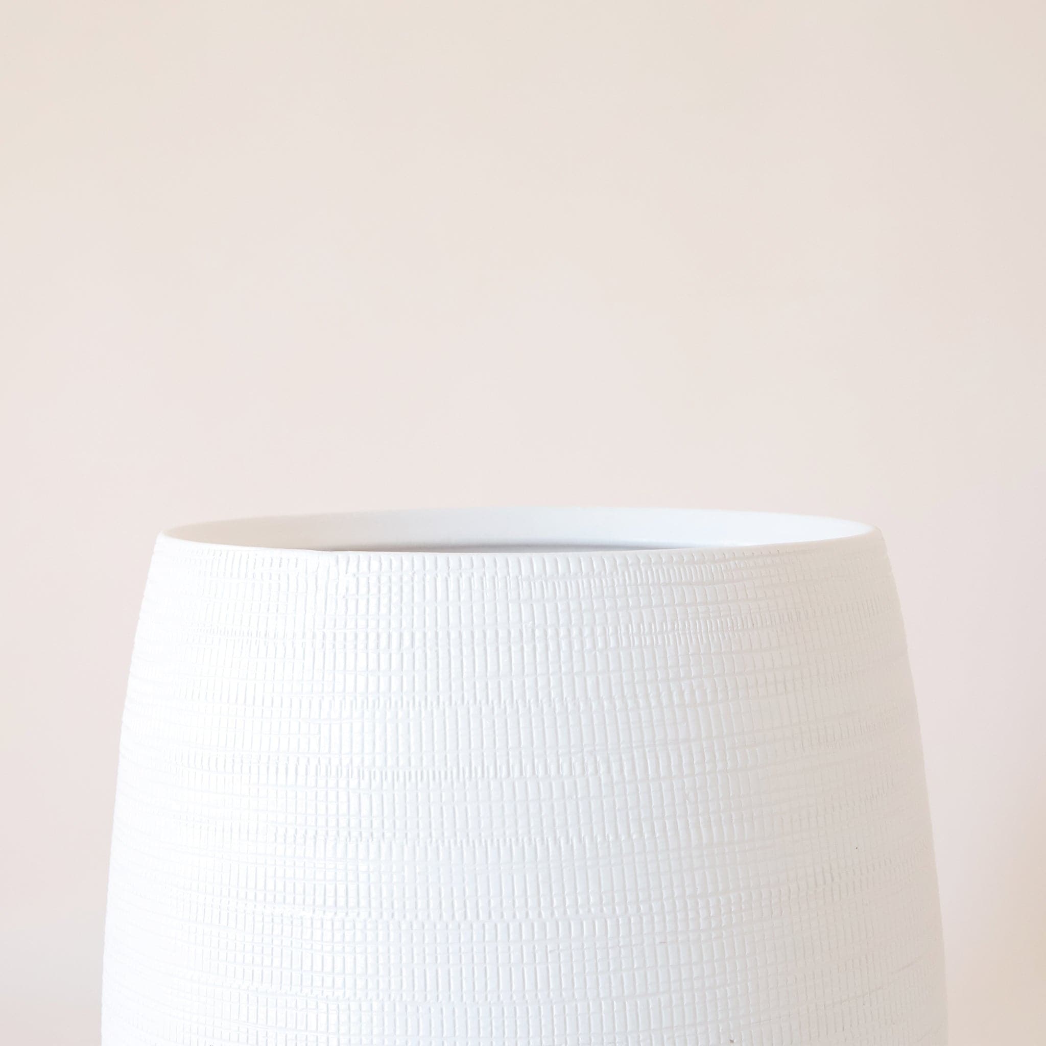 On a cream background is a white rounded ceramic pot with a tiny rectangular texture all over.