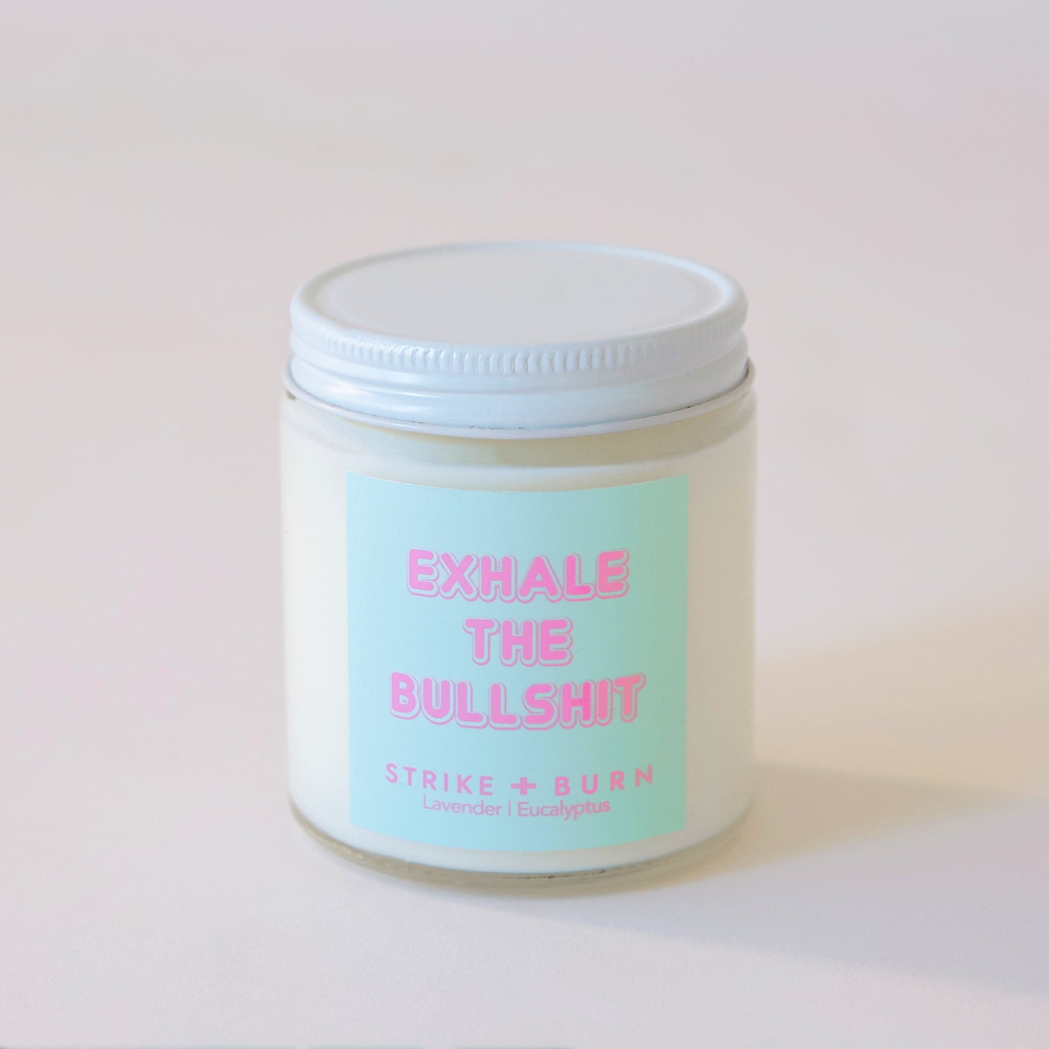 Clear, glass jar candle with white metal lid. Label says &quot;Exhale the bullshit&quot; in pink with a aqua colored background.