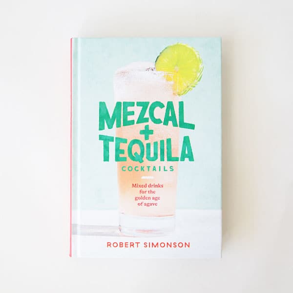 A light blue book cover with a pink tropical cocktail on the front with the title, &quot;Mezcal + Tequila Cocktails&quot; in teal blue lettering.