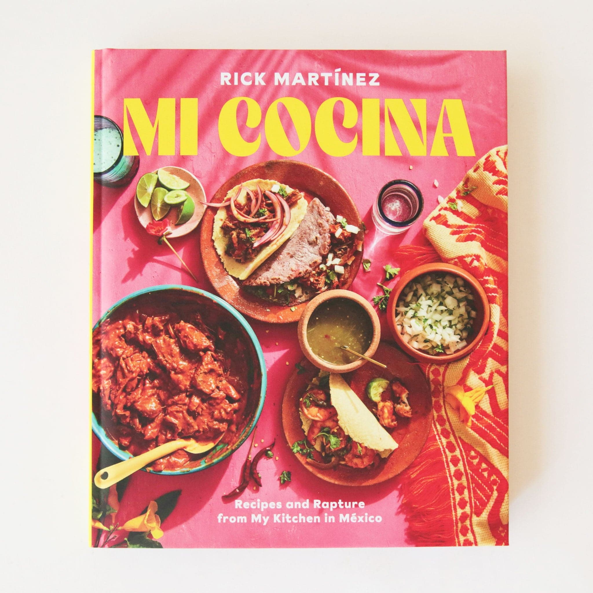 A bright pink book cover with a yellow font title that reads, "Mi Cocina" along with an assortment of Mexican cuisine.