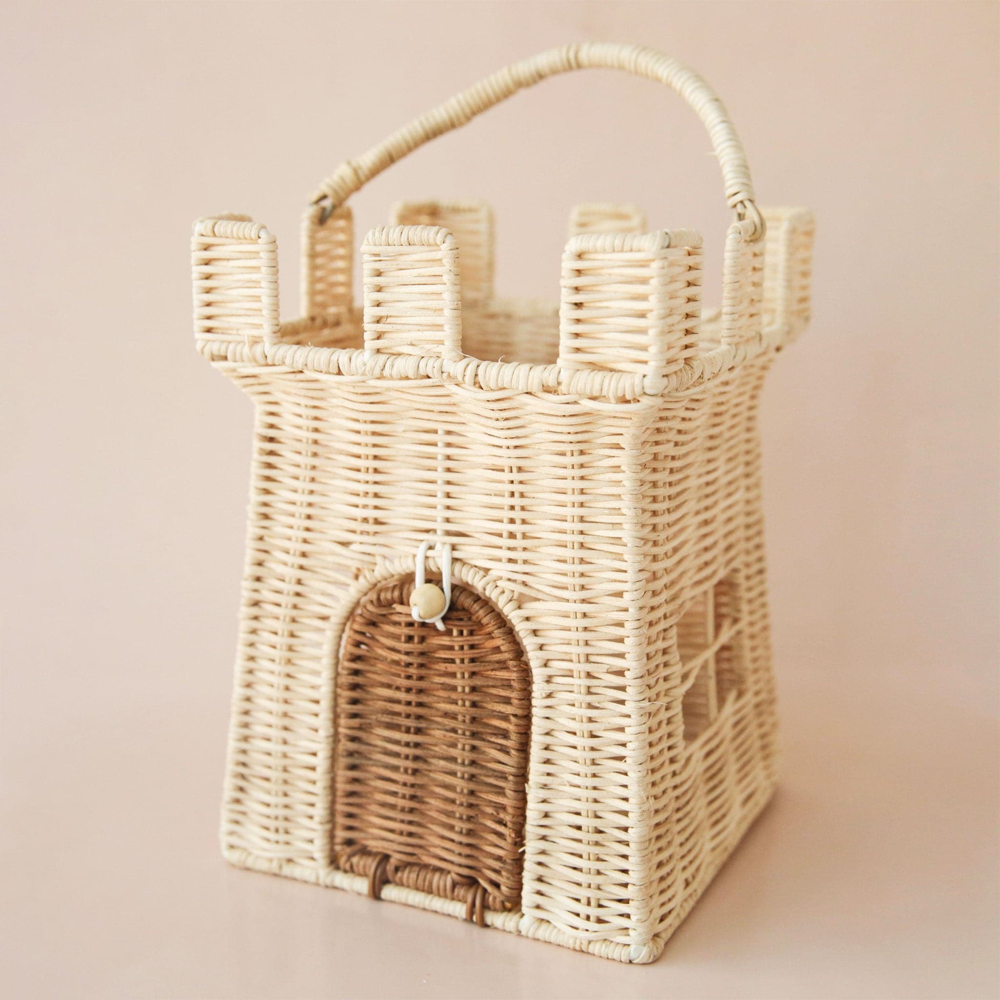 A wicker castle shaped basket with an open top as well as an opening where the door of the castle is. Also included is an attached handle for carrying around.