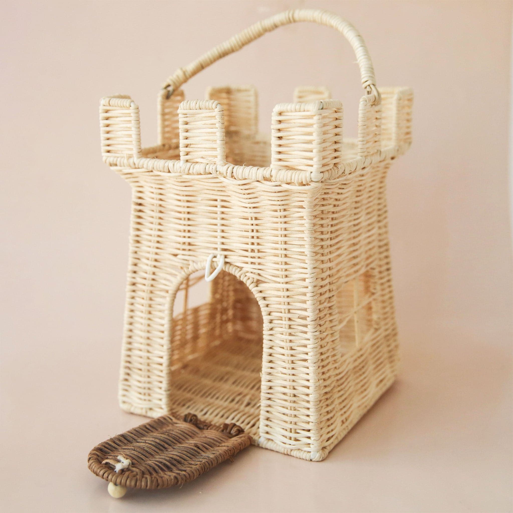 A wicker castle shaped basket with an open top as well as an opening where the door of the castle is. Also included is an attached handle for carrying around.