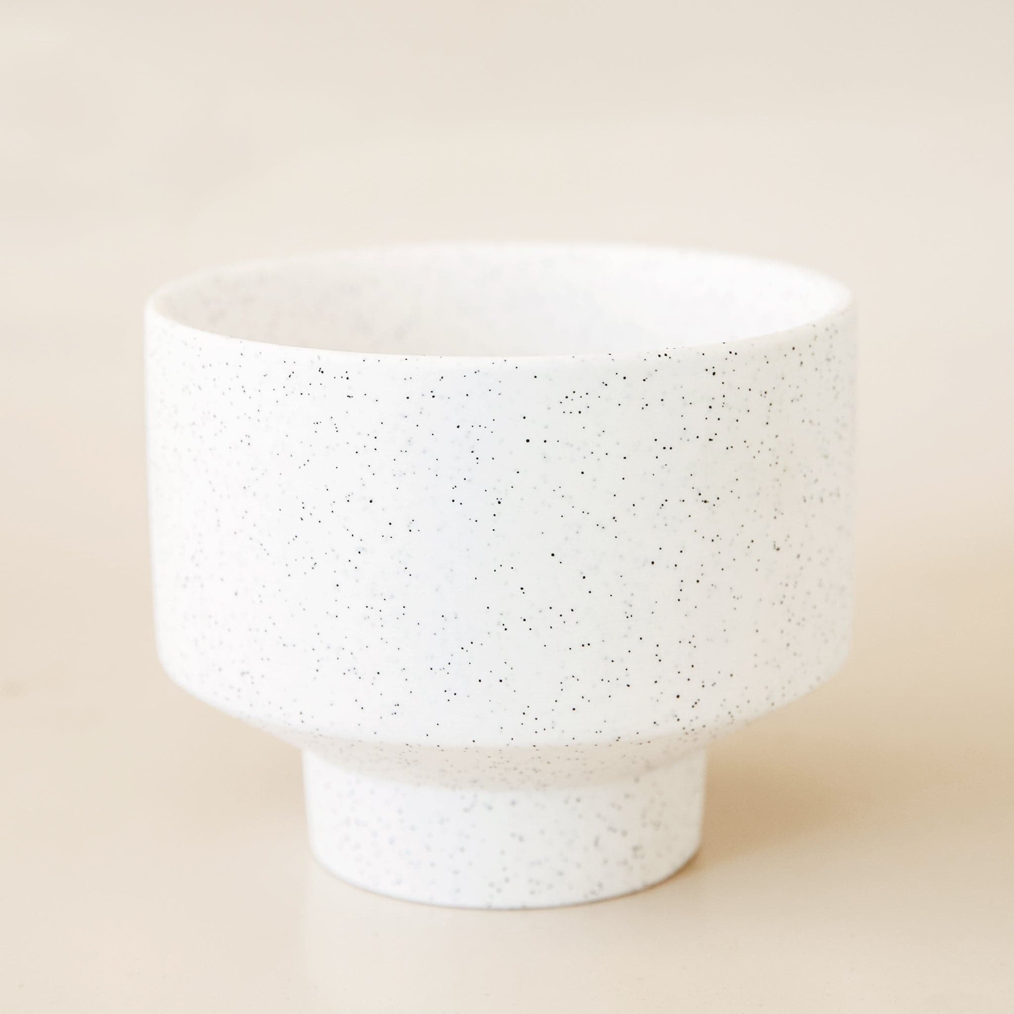 White cylinder pot that tapers into a smaller base. The pot is covered in black speckles.