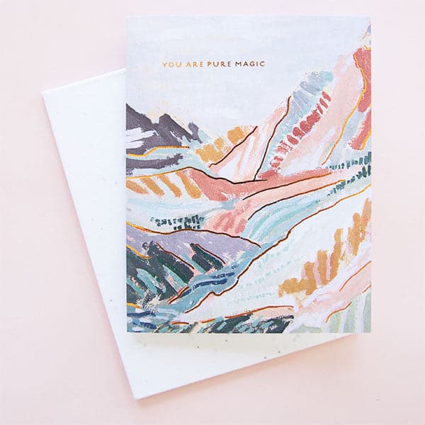 A multi colored illustration of a mountain scape with shades of rust, dark turquoise and mustard yellows along with tiny text at the top of the card that reads, "You Are Pure Magic" in gold foiled lettering. 