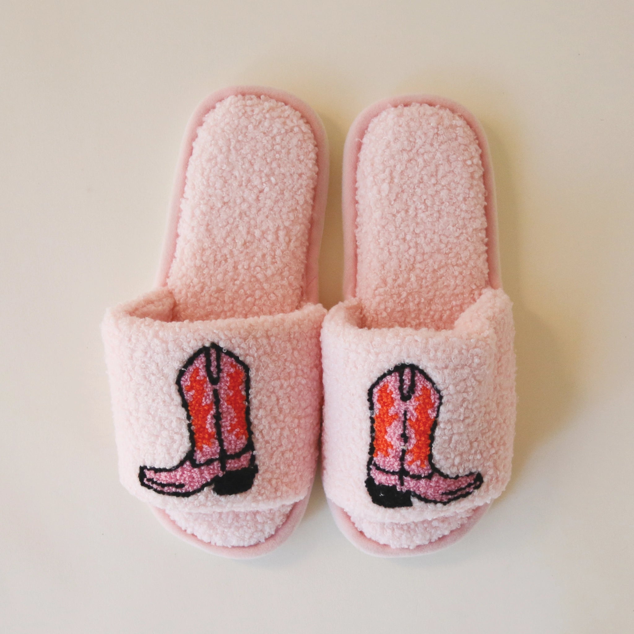 Pink fuzzy slide slippers with an open toe front and a pink and red cowgirl boot graphic on the top.