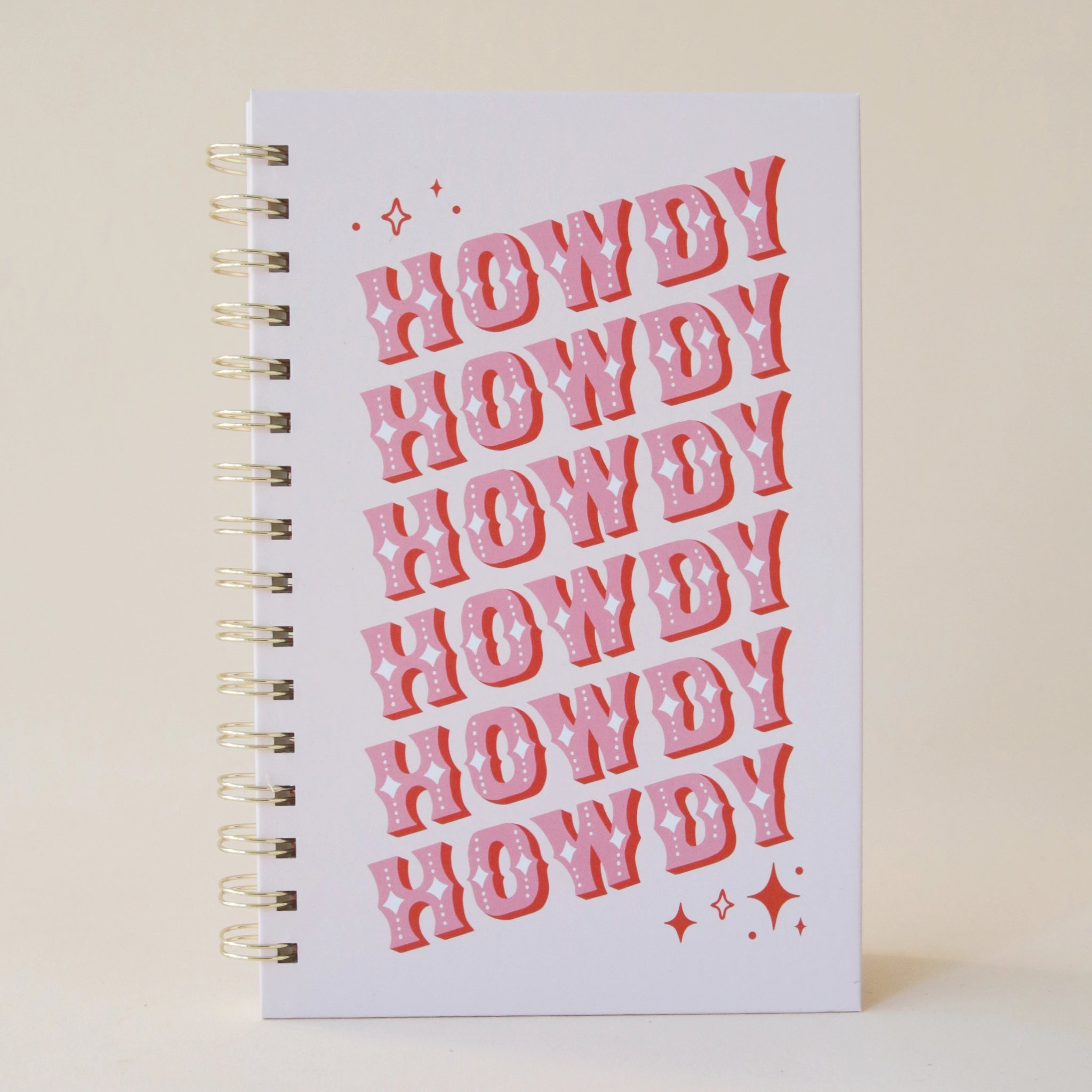 A light purple / cool toned pink notebook with the word "Howdy" slightly angled and stacked six times in pink western font and featuring a spiral bound detail.