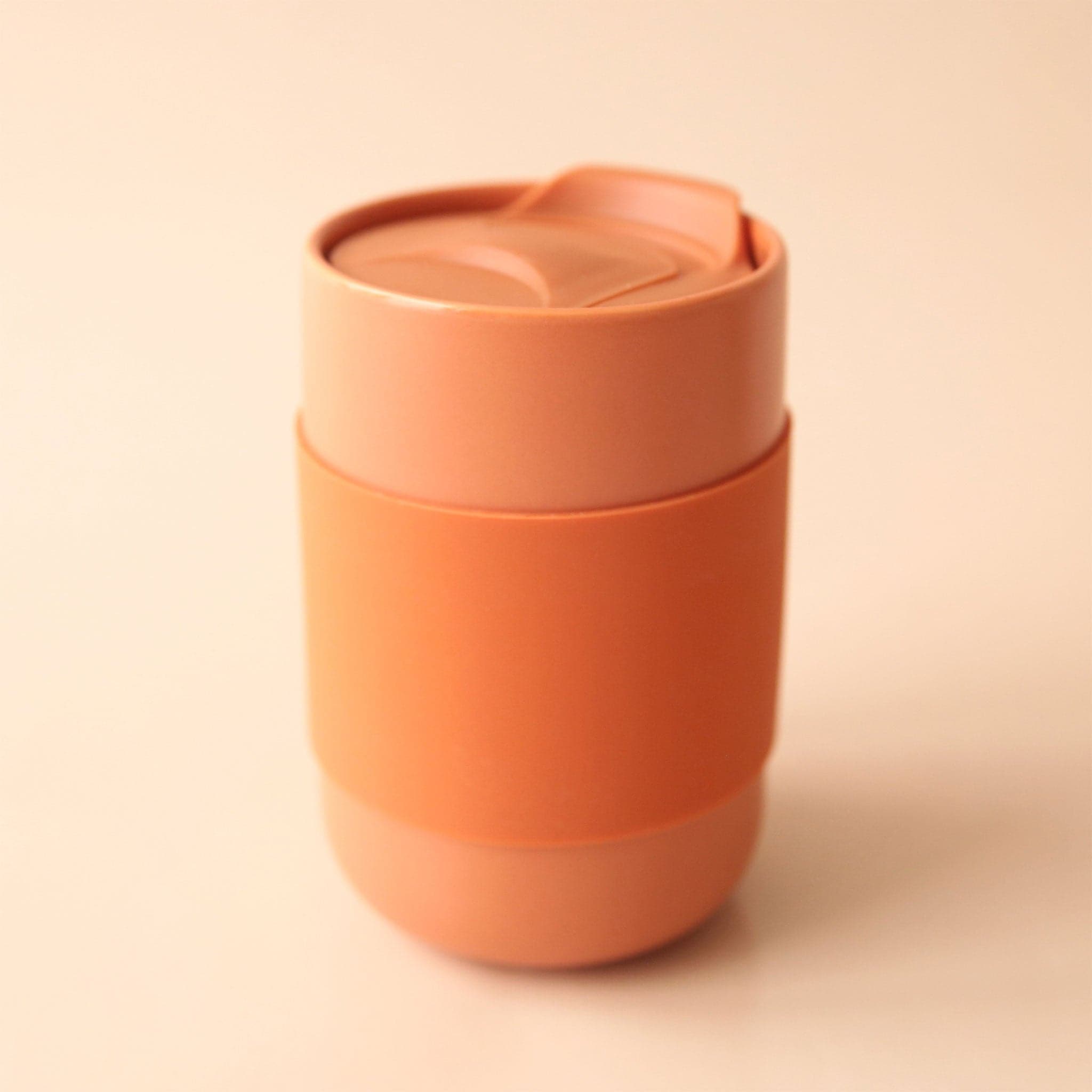 A terracotta travel cup made of dishwasher safe ceramic along with a removable silicone sleeve.