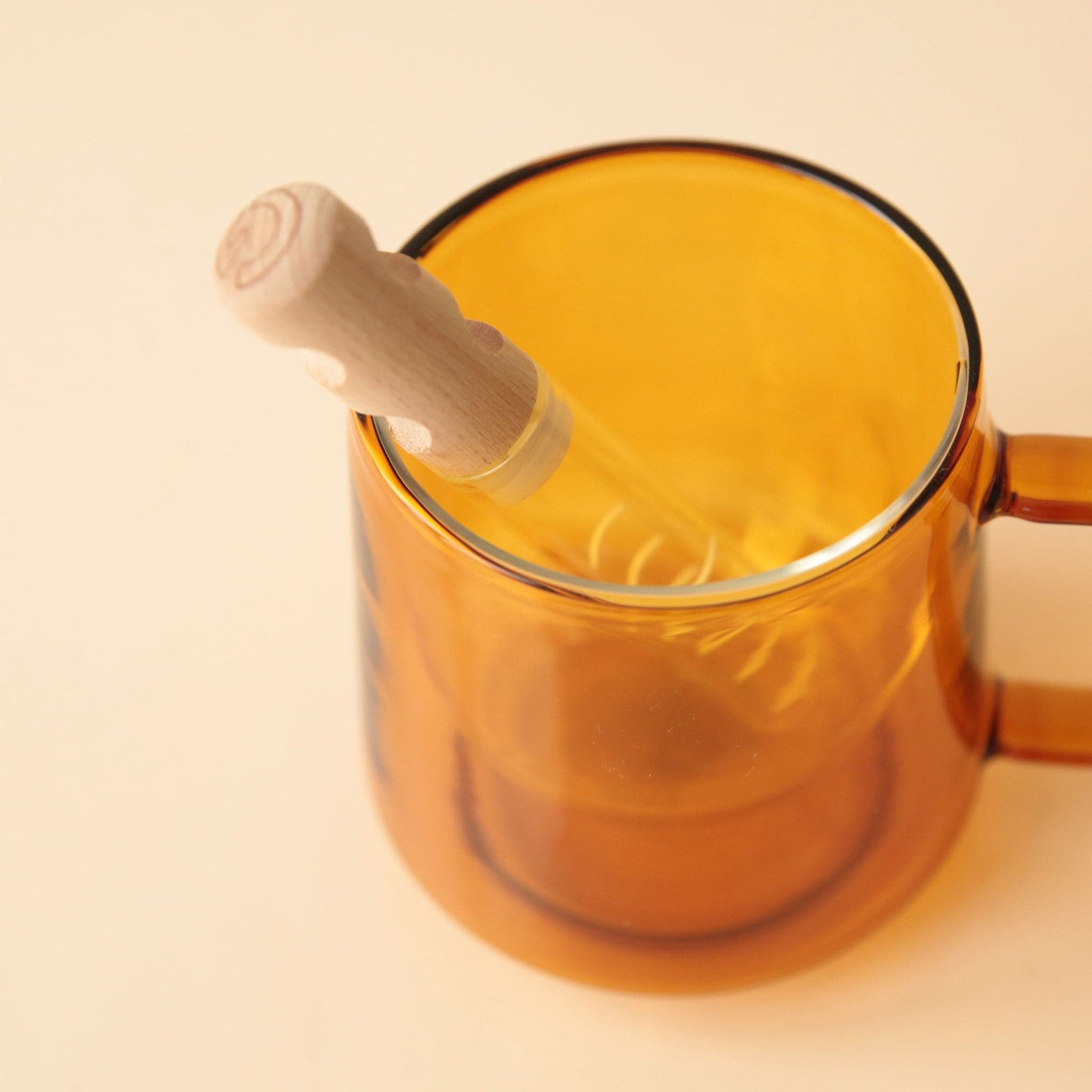 A glass tea infusing stick with 4 slender openings that allow water to seep in and infuse. The cap is made of silicone and bamboo staged inside of a glass mug. 