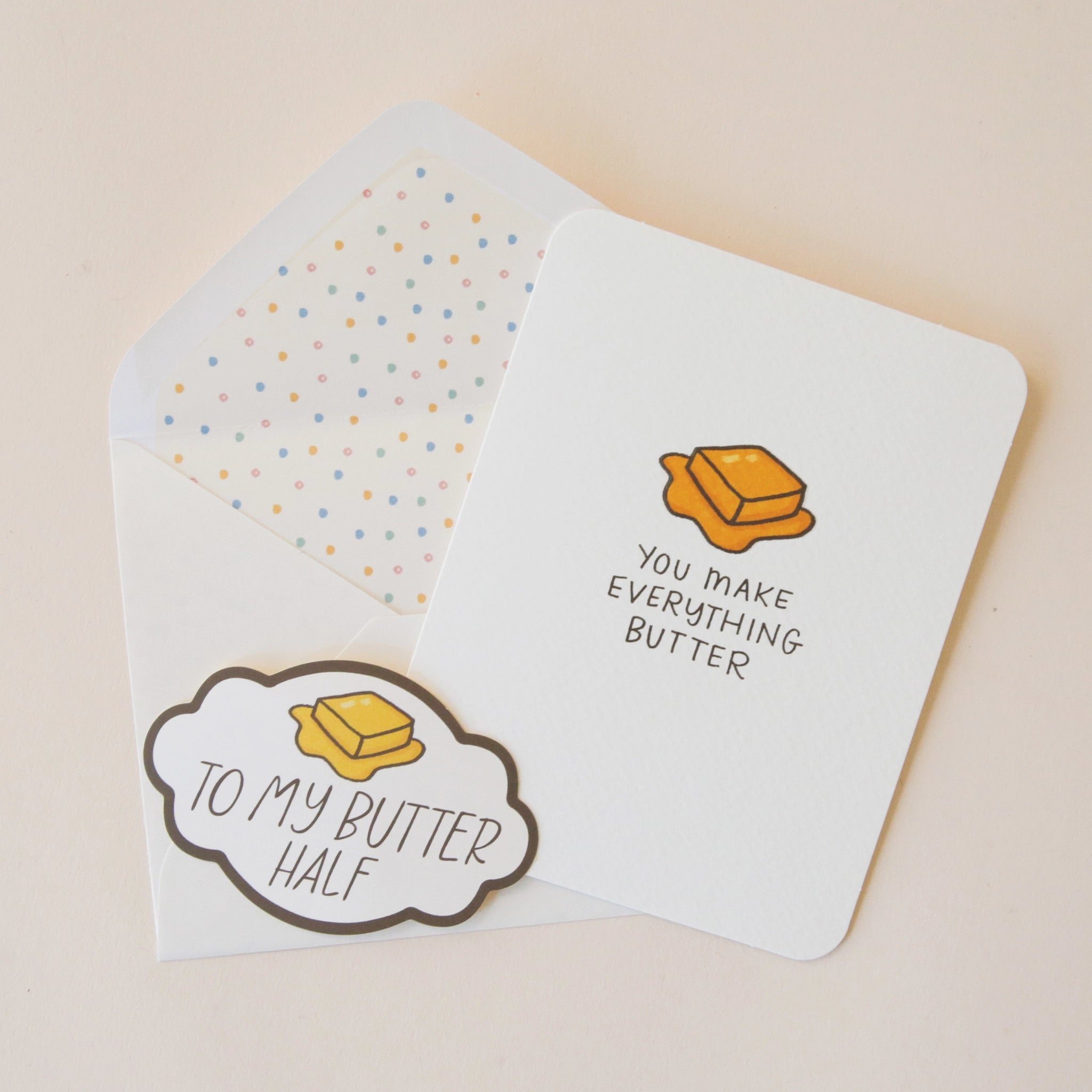 A white card with a slice of yellow butter graphic and black text that reads &quot;You Make Everything Butter&quot; along with a coordinating sticker that is included and has bubble edges and has a similar butter illustration and says, &quot;To My Butter Half&quot;.