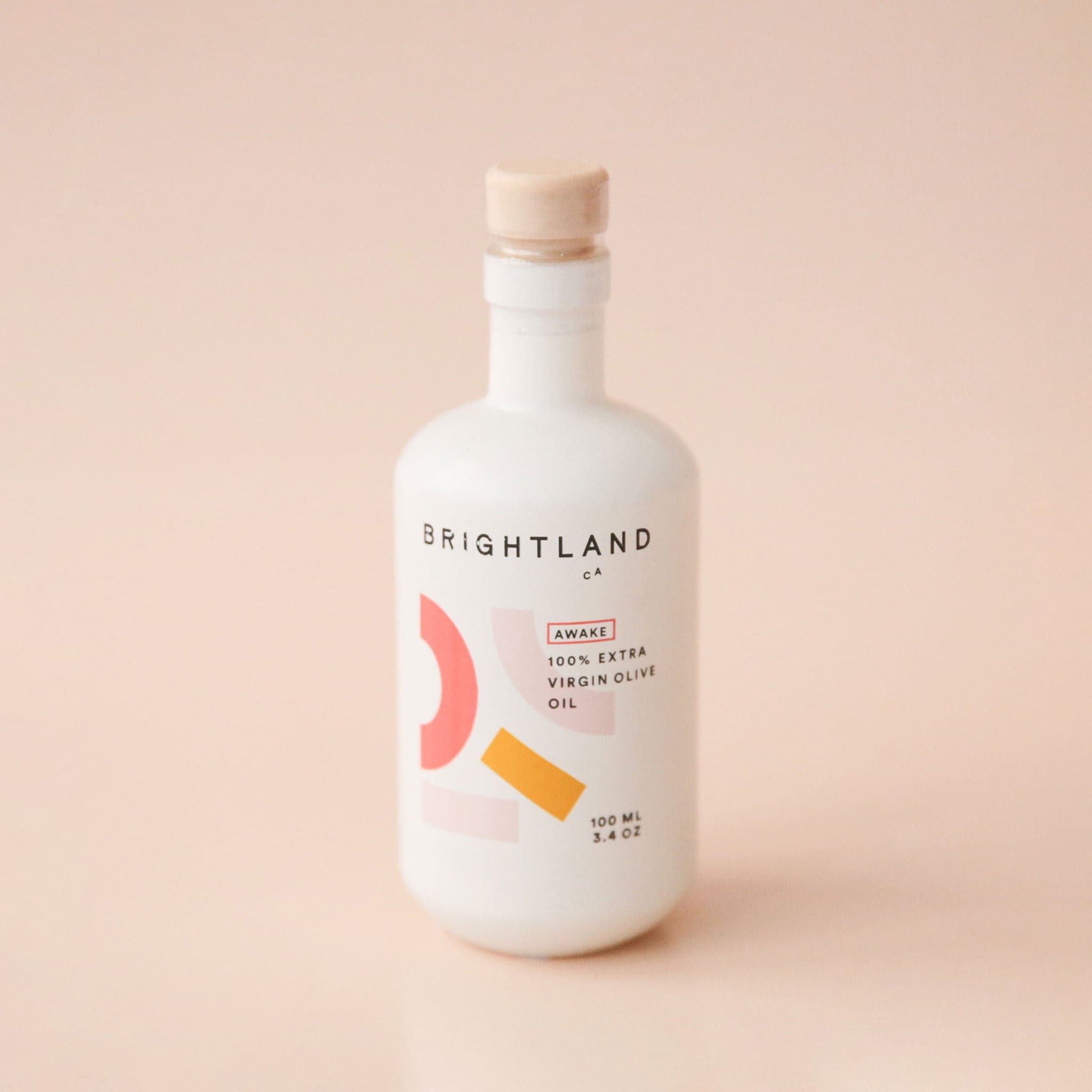 A white opaque bottle with light brown stopper and label with text &quot;Brightland. LA California Made. Awake. 100% Extra Virgin Olive Oil. For cozy days and slow nights.&quot;