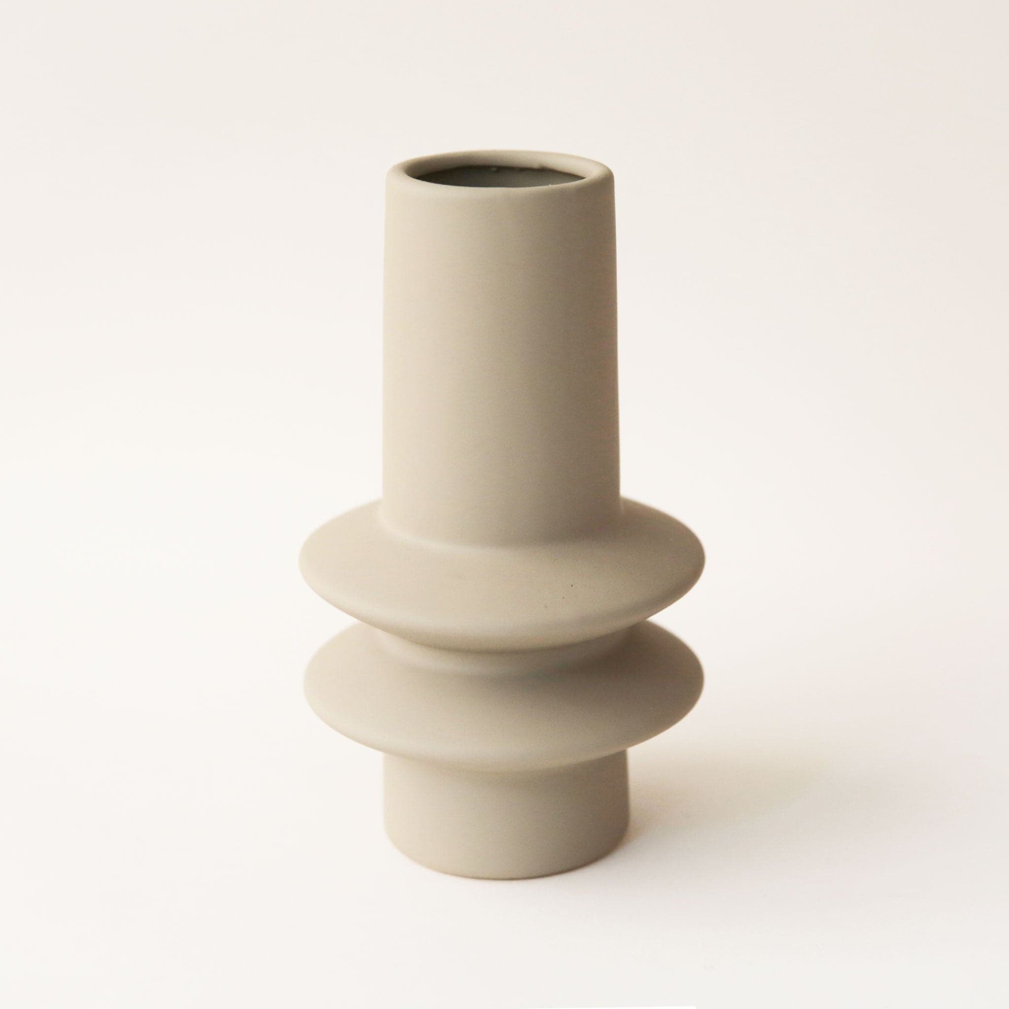 A thin ceramic vase in a beige shade with two saucer like shapes toward the bottom half of the vase along.