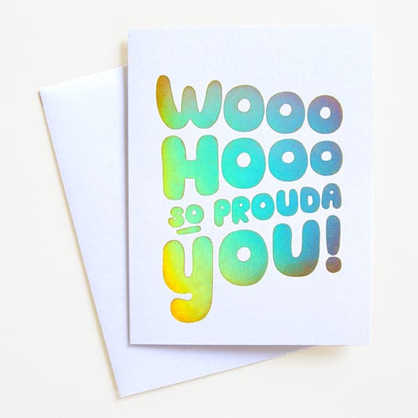 On top of a white envelope is a white card with silver holographic text that reads ‘woo hoo so prouda you!'
