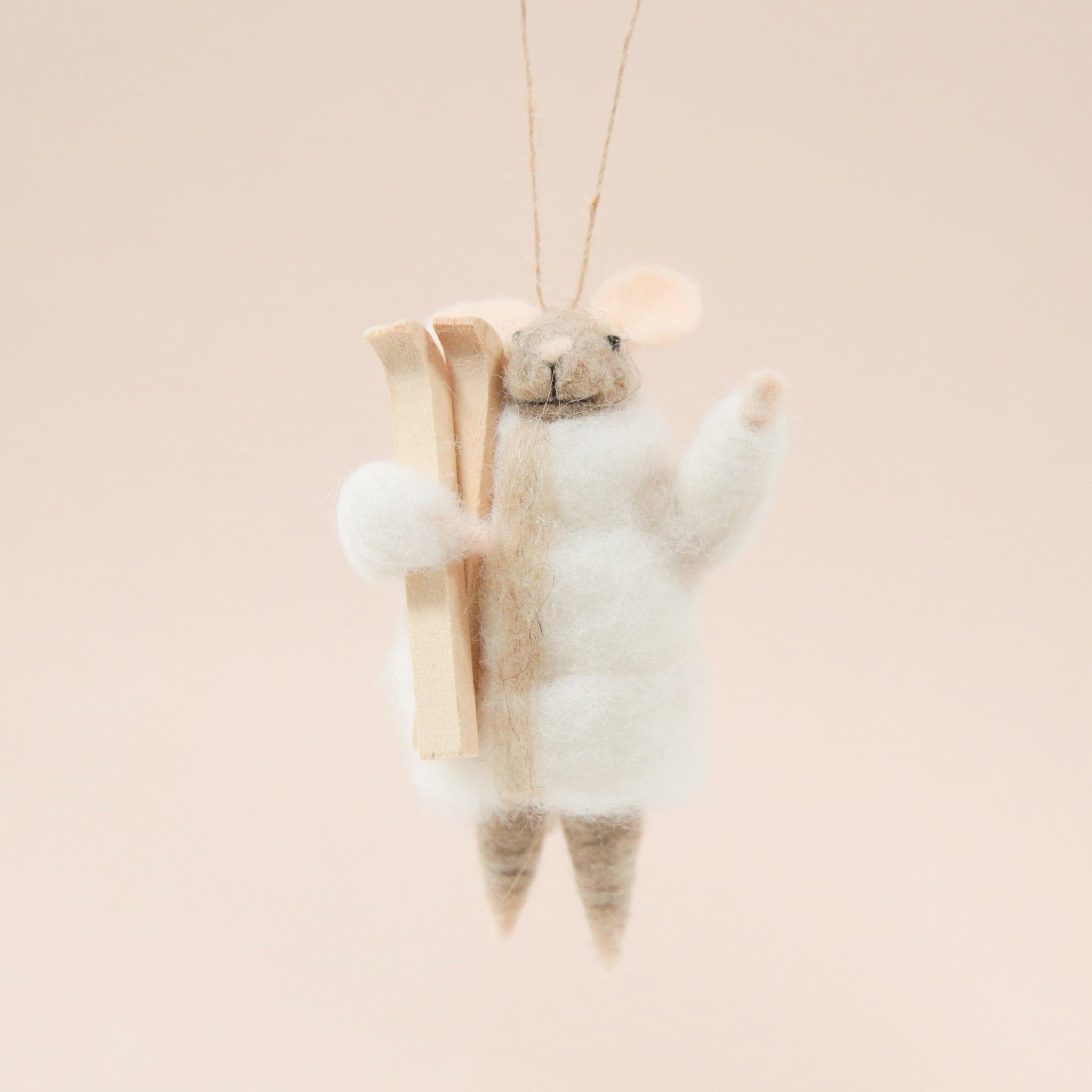 On a light tan background is a brown felt mouse ornament with a white jacket and a pair of a wood skis.