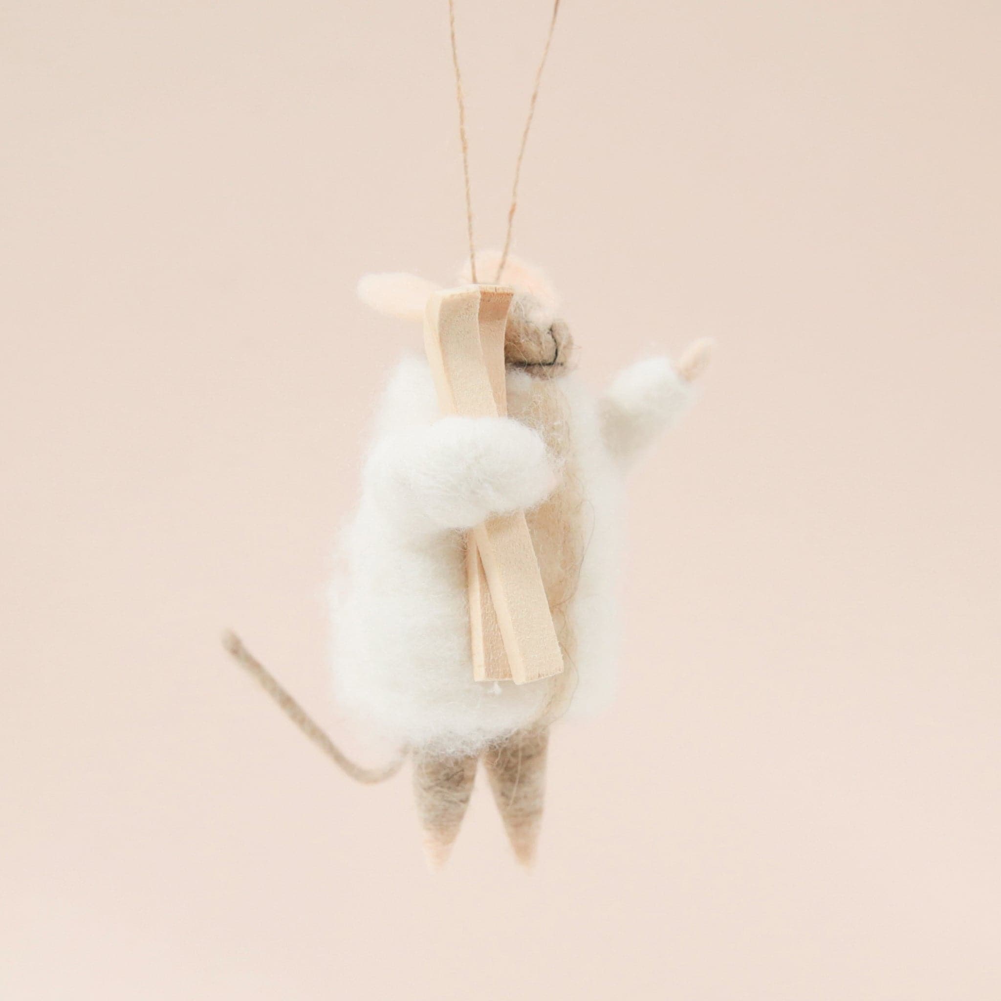 On a light tan background is a brown felt mouse ornament with a white jacket and a pair of a wood skis.