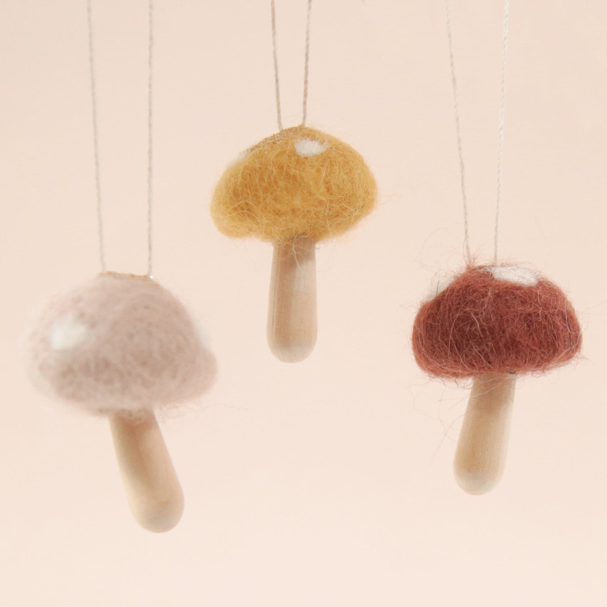 A cocoa colored mushroom ornament with white spots and a light wood stem. photographed here with the other two available color ways which come in a light mauve and mustard shade.