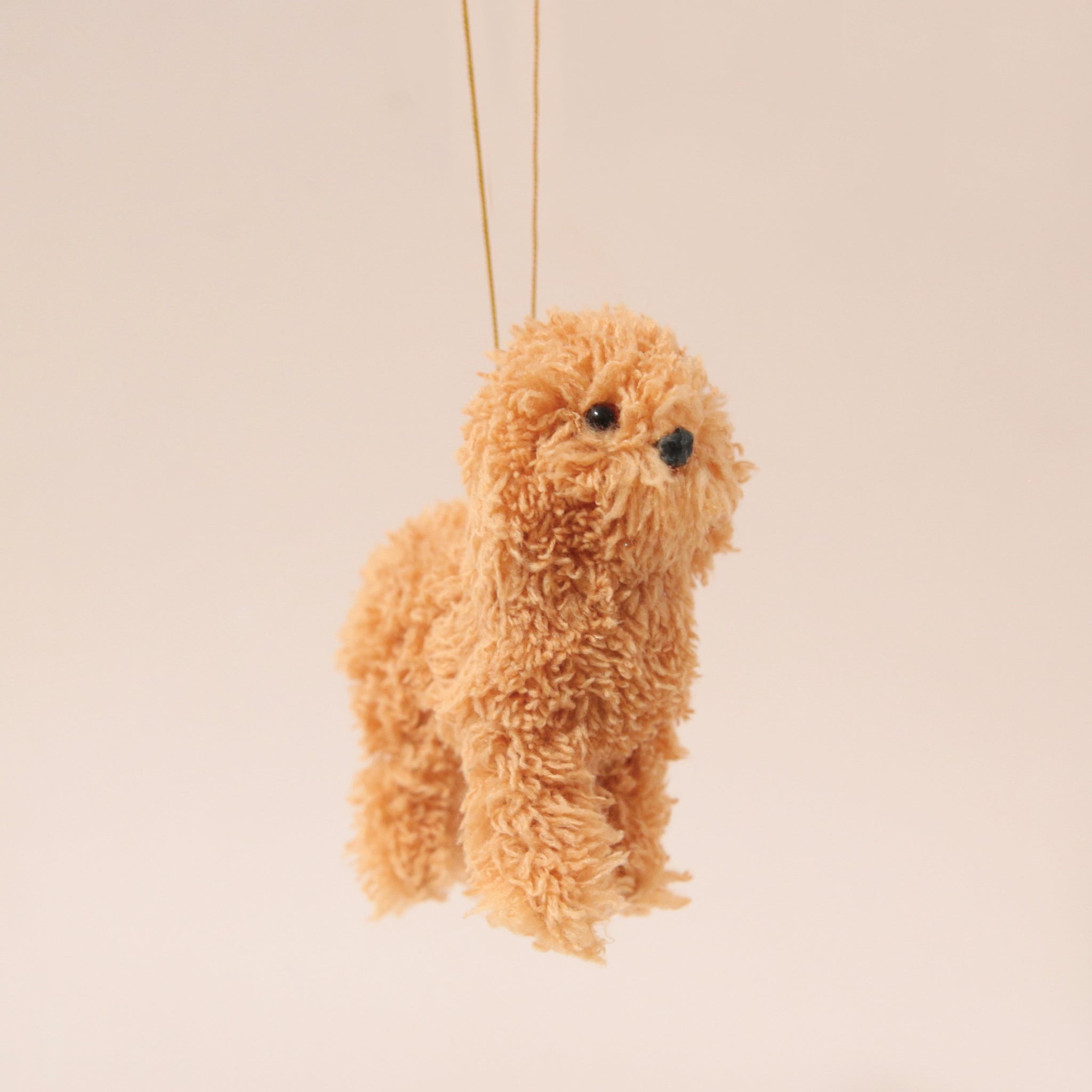 A caramel furry poodle ornament with a gold loop for hanging.