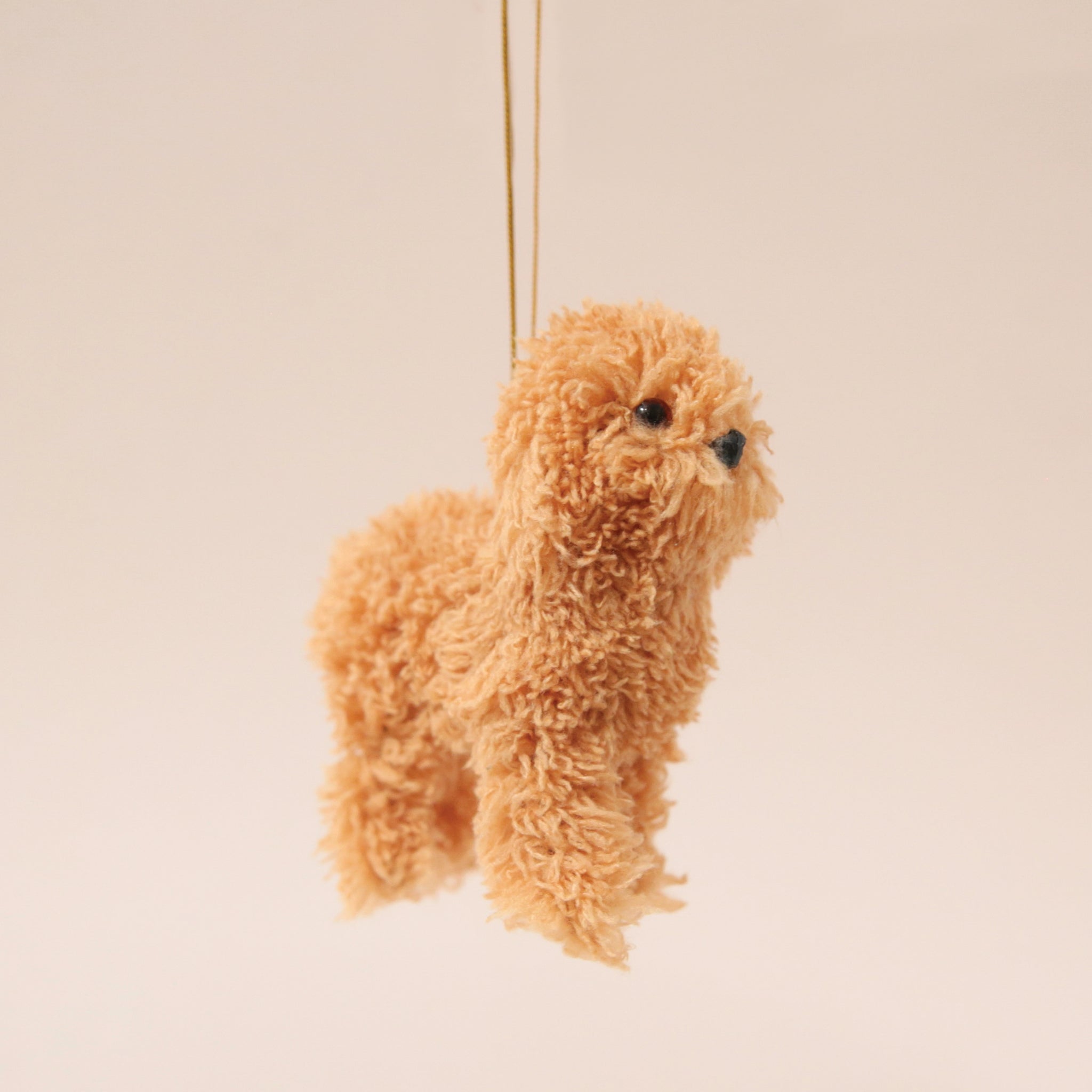 A caramel furry poodle ornament with a gold loop for hanging.