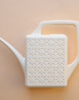 An ivory plastic watering can with a narrow spout and square handle and a rectangle breeze block design on the sides.