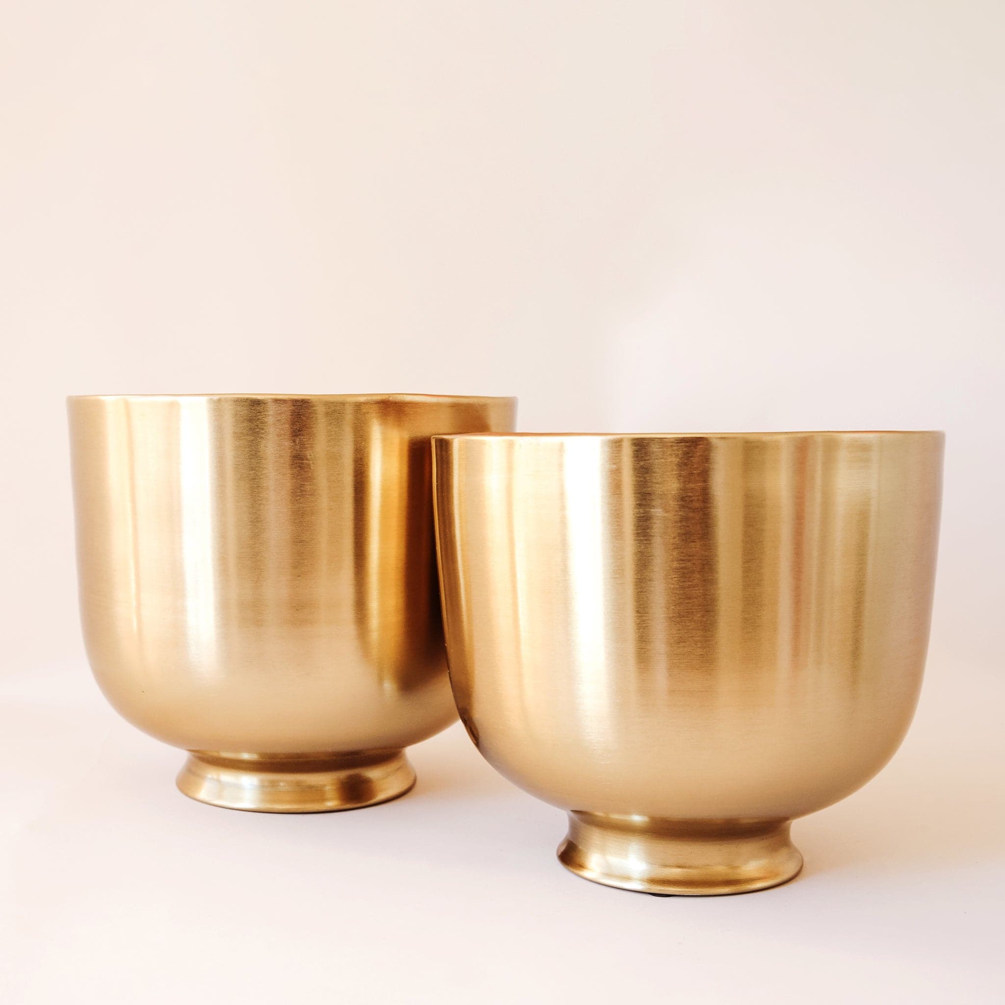 The sunglow planter has a gold metal finish, making it reflective to the light. It has a round shape with a tapered bottom. 