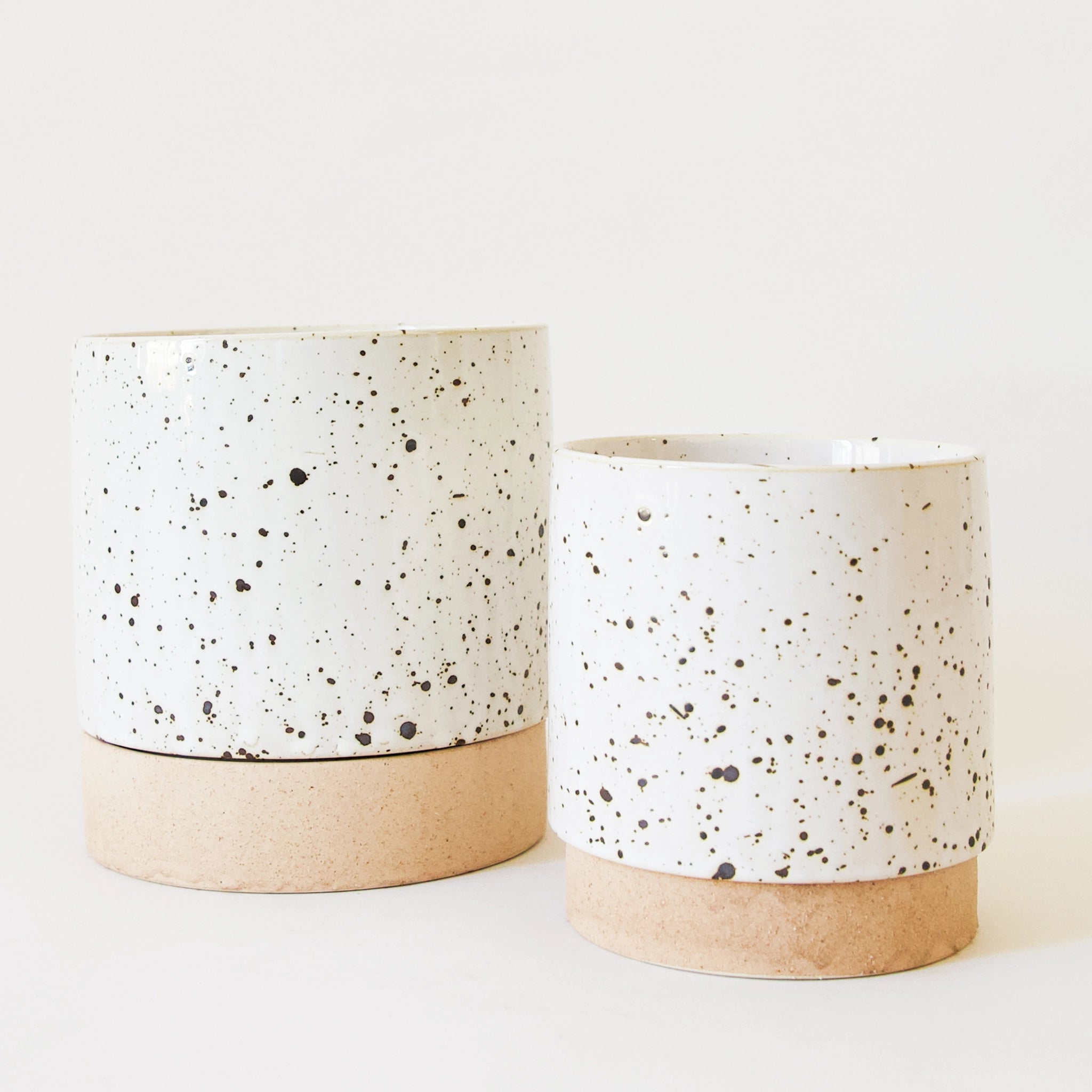 two pots, a small and large, feature dark speckles on a white glaze finish. both have a stoneware base.