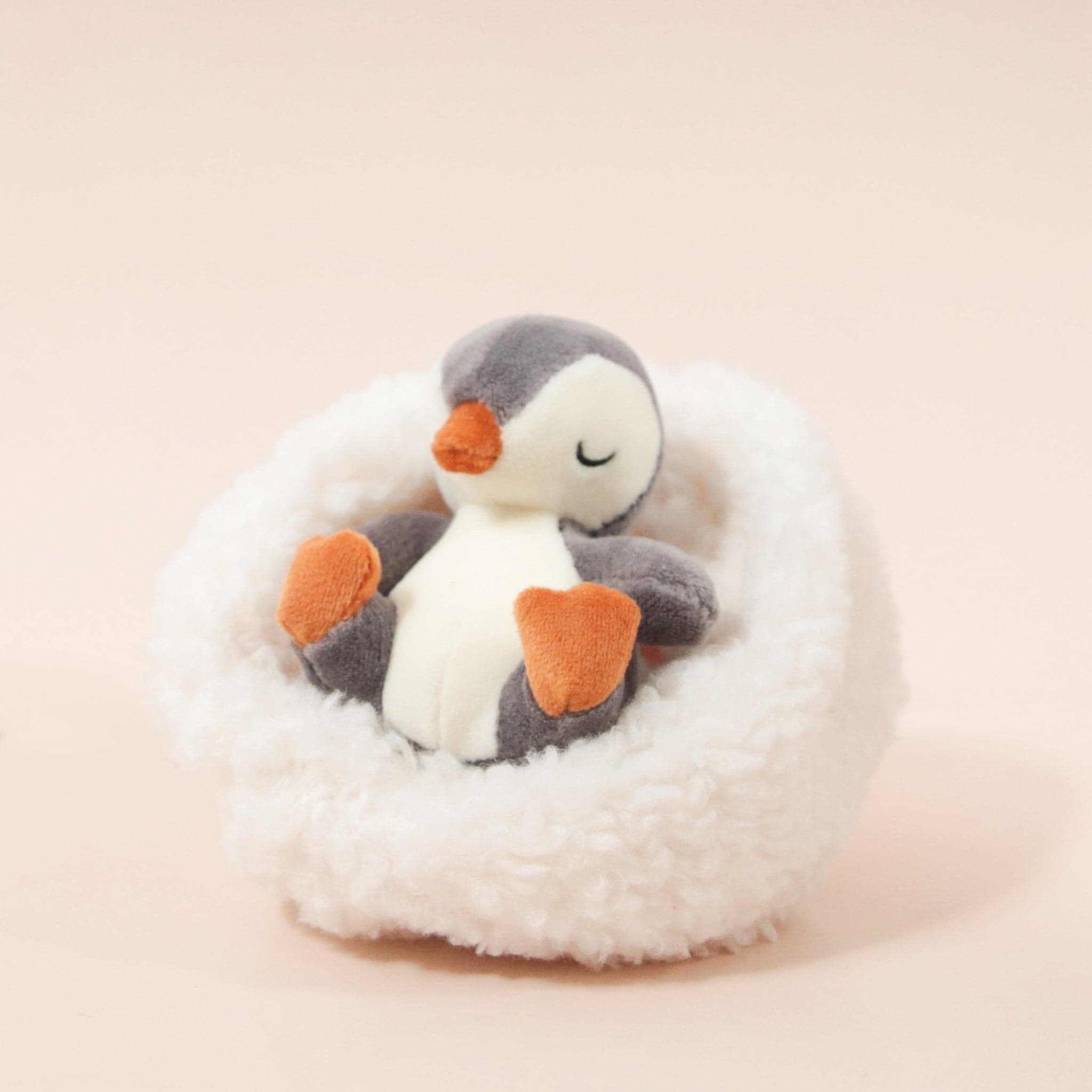 On a cream background is a penguin stuffed animal with a white boucle bed.