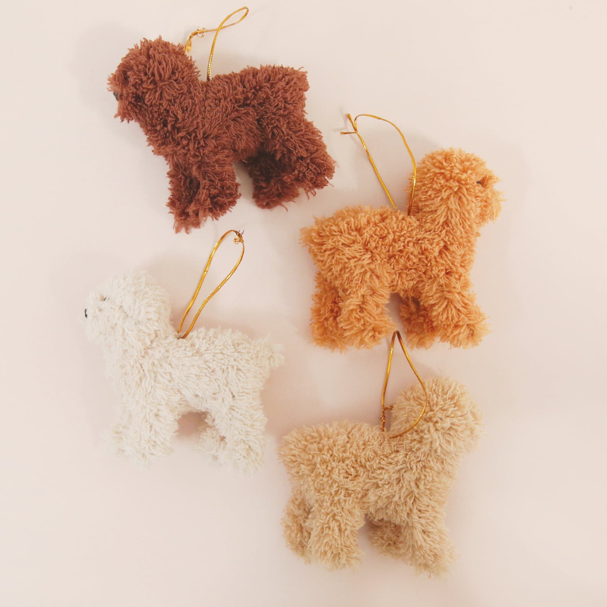 On a tan background is four different colors of furry poodle ornaments.