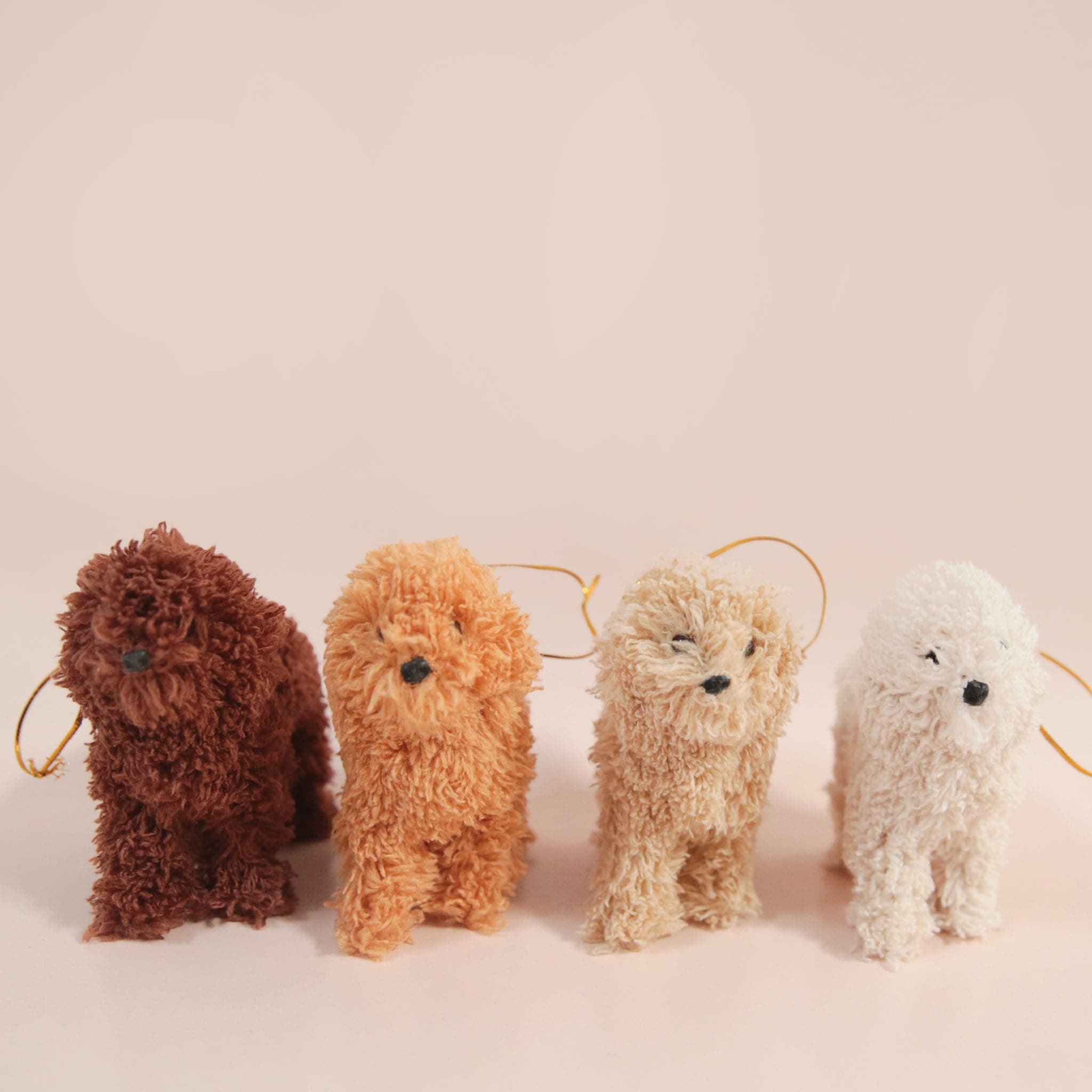 On a tan background is four different colors of furry poodle ornaments.