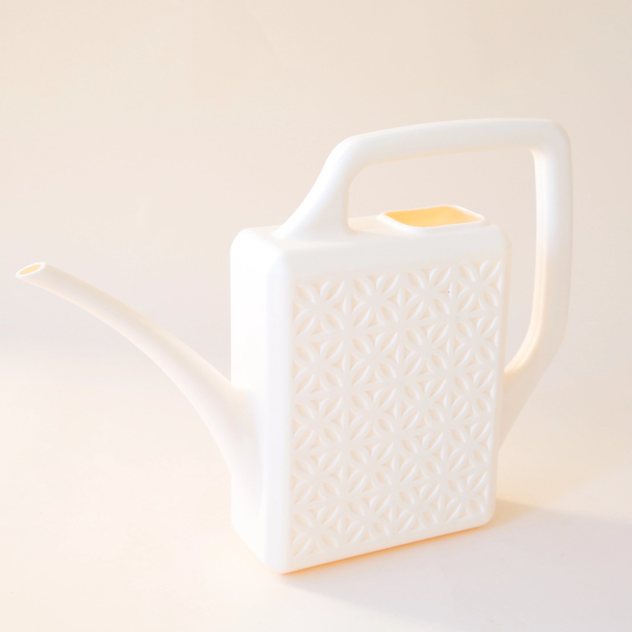 An ivory plastic watering can with a narrow spout and square handle and a rectangle breeze block design on the sides.