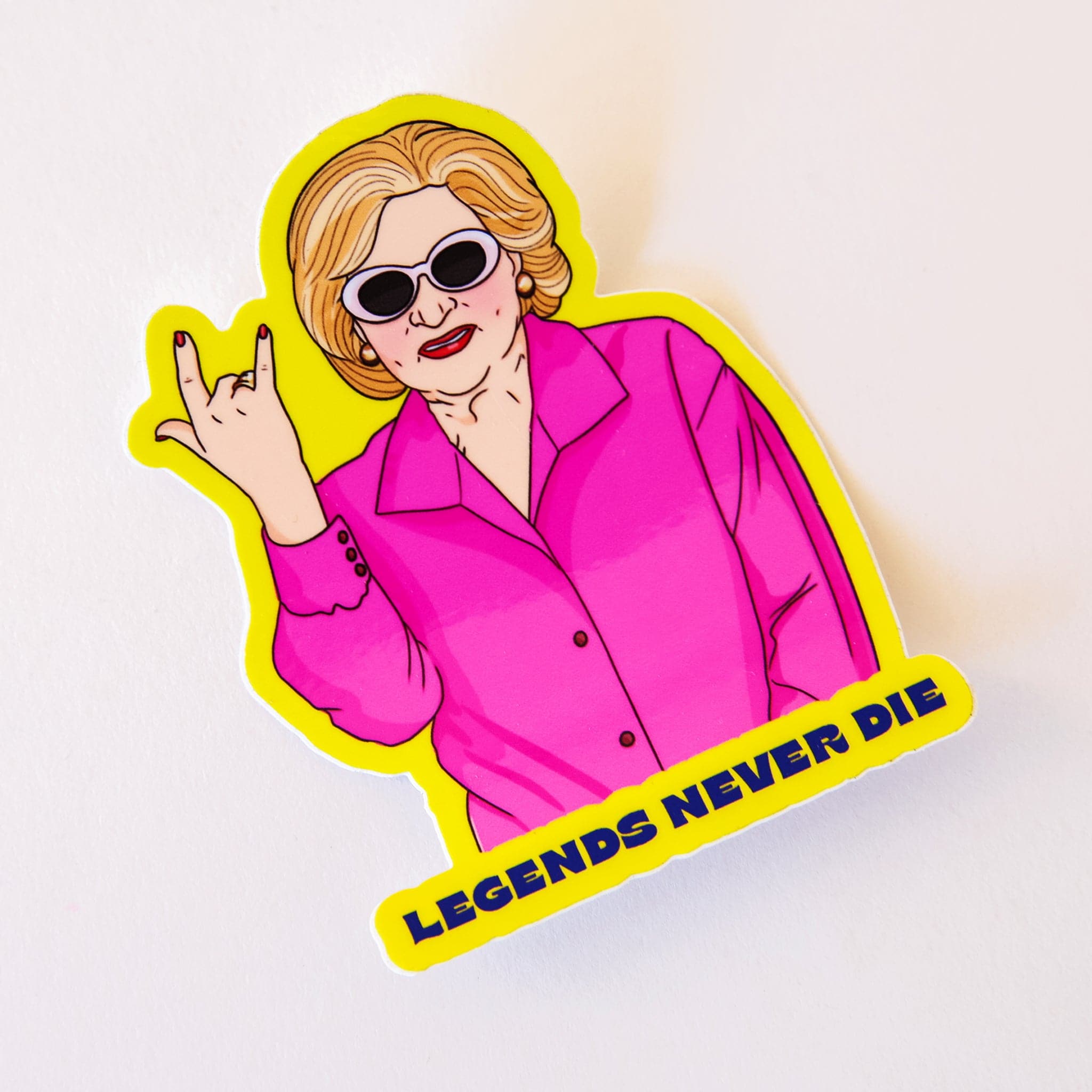  A sticker of Betty White throwing up a rocker sign  wearing clout goggles with font that reads, "Legends Never Die".