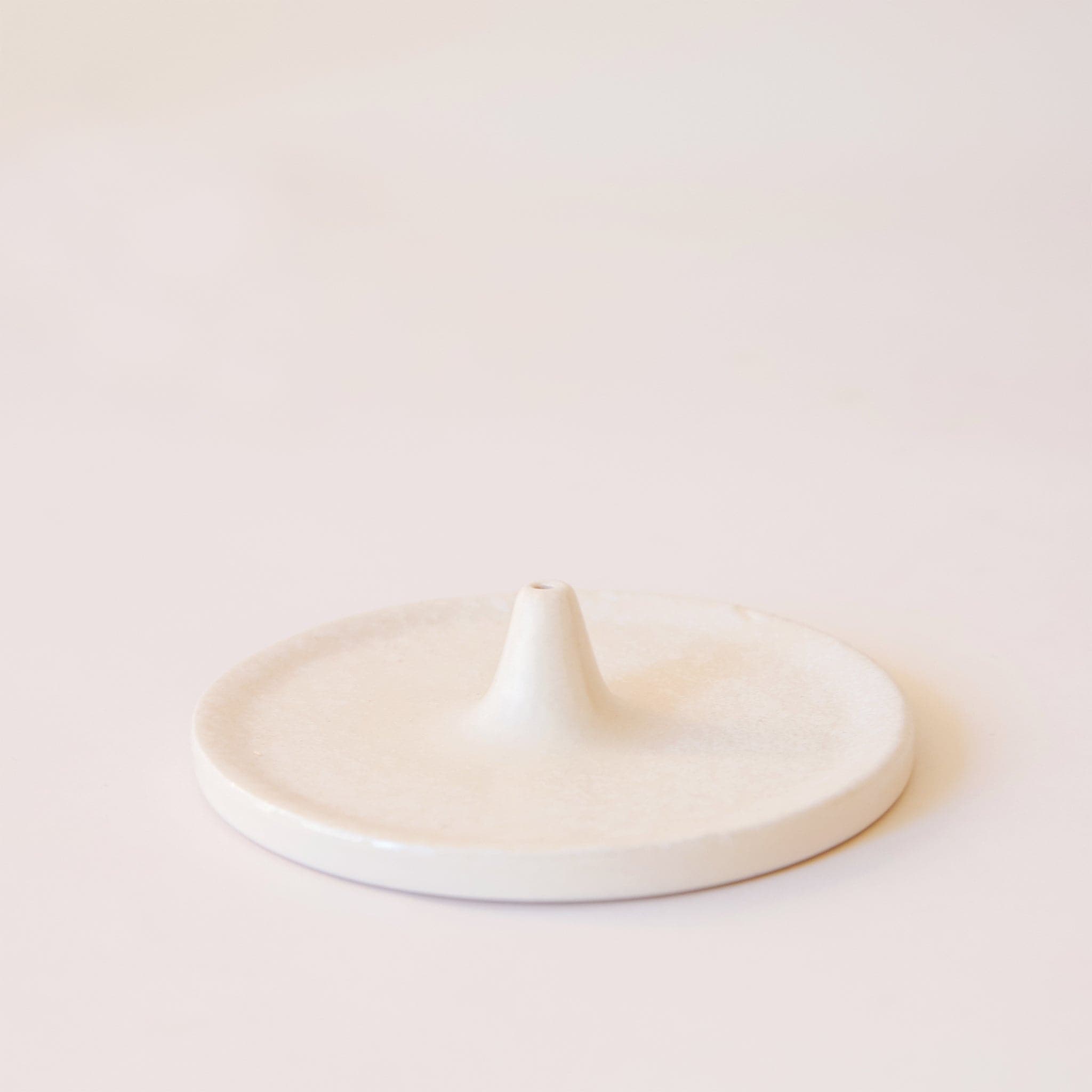 A white incense holder that has a circular shape with a point in the center that is raised with a hole to place your incense in.