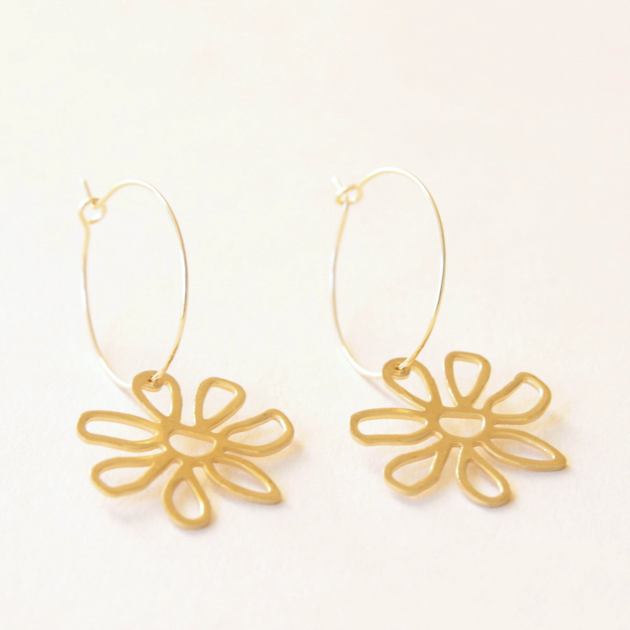 On a cream background is the smaller sized hoop gold earrings with the same flower charm hanging off the bottom of the hoop.  