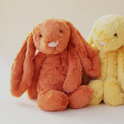 A vibrant dark orange stuffed animal bunny with fuzzy fur, long floppy ears, a light pink nose and black eyes.