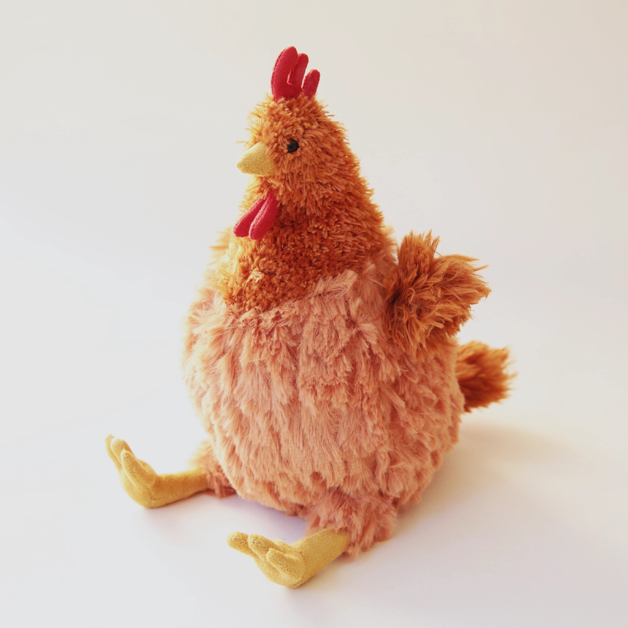 A chicken stuffed animal with vibrant orange and fur and red and yellow detailing. It has a yellow beak and yellow feet.